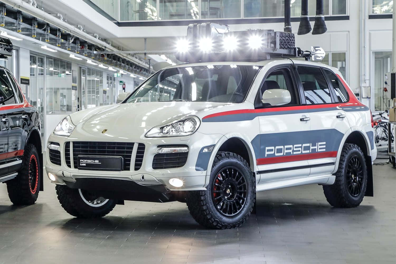Off-road Car 桌布 壁紙 — 一輛白色保時捷Cayenne帶有紅藍賽車條紋和車頂燈，停在明亮的工業車庫中。