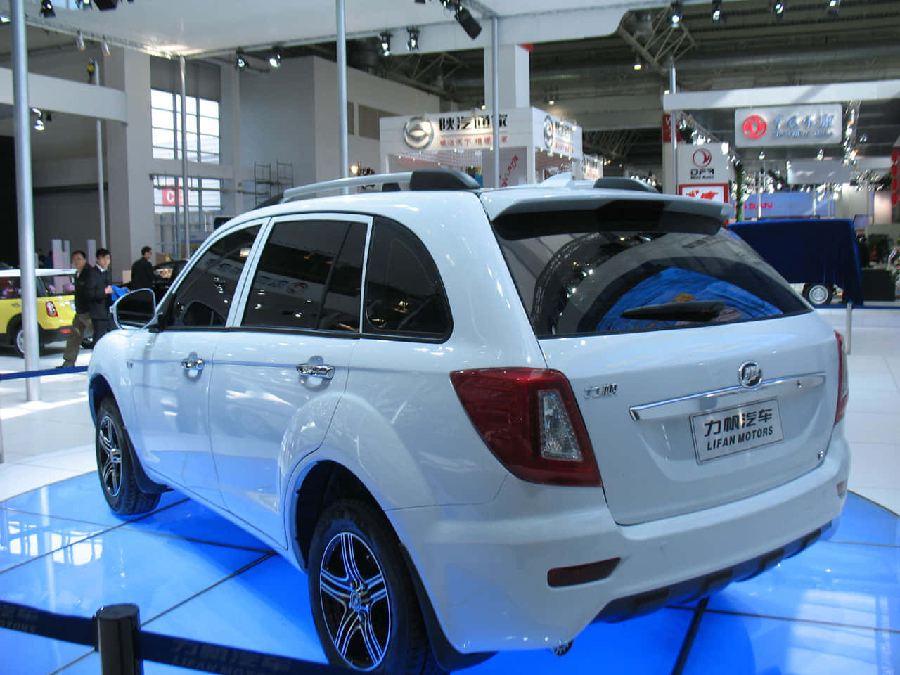 Lifan 桌布 壁紙 — 一輛白色力帆SUV在藍色展台上於車展中展示，上方有明亮燈光，背景有模糊的與會者。