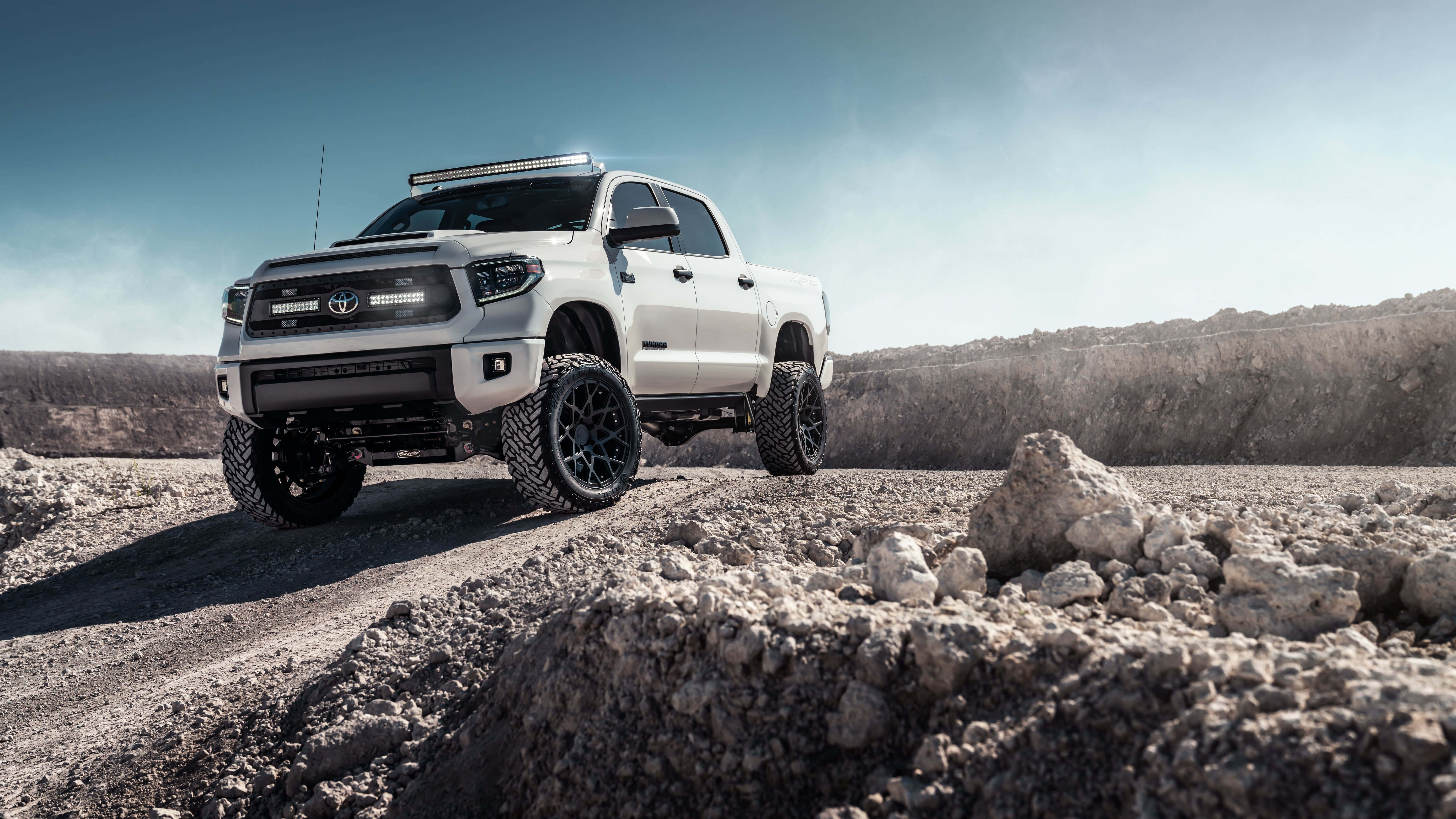 Toyota 桌布 壁紙 — 一輛白色升高底盤的豐田Tundra貨車，配備黑色輪圈，在晴朗藍天下征服岩石地形。