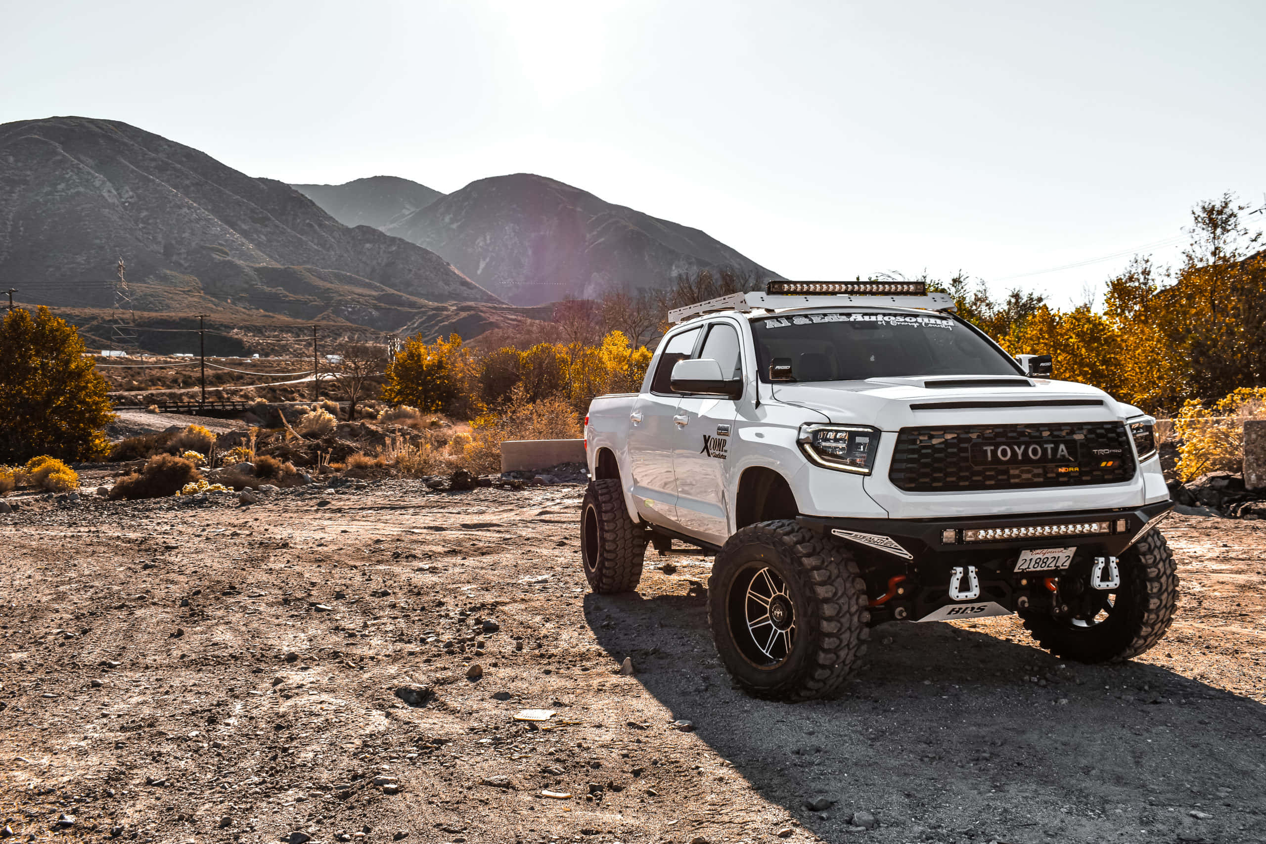 Toyota 桌布 壁紙 — 一輛白色升高的豐田 Tacoma 在陽光明媚的沙漠中準備好越野，背景是崎嶇的山脈。