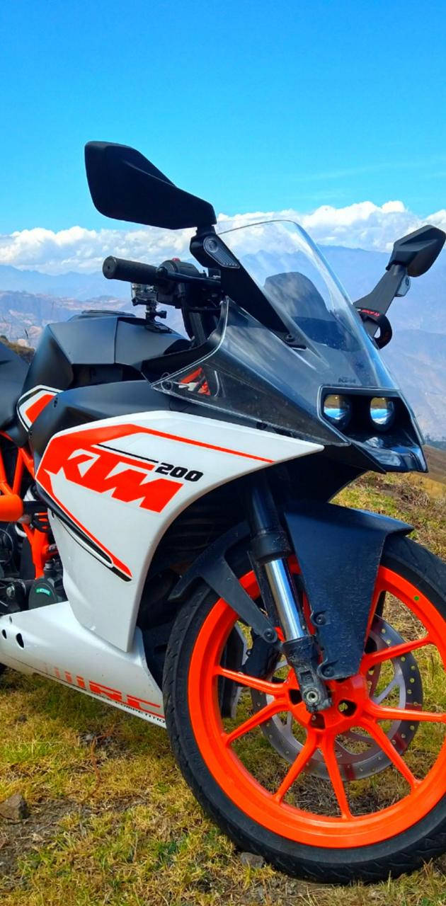 KTM RC 200 桌布 壁紙 — 一輛白色和橙色的KTM 200機車停在草地上，背景有山脈和藍天。