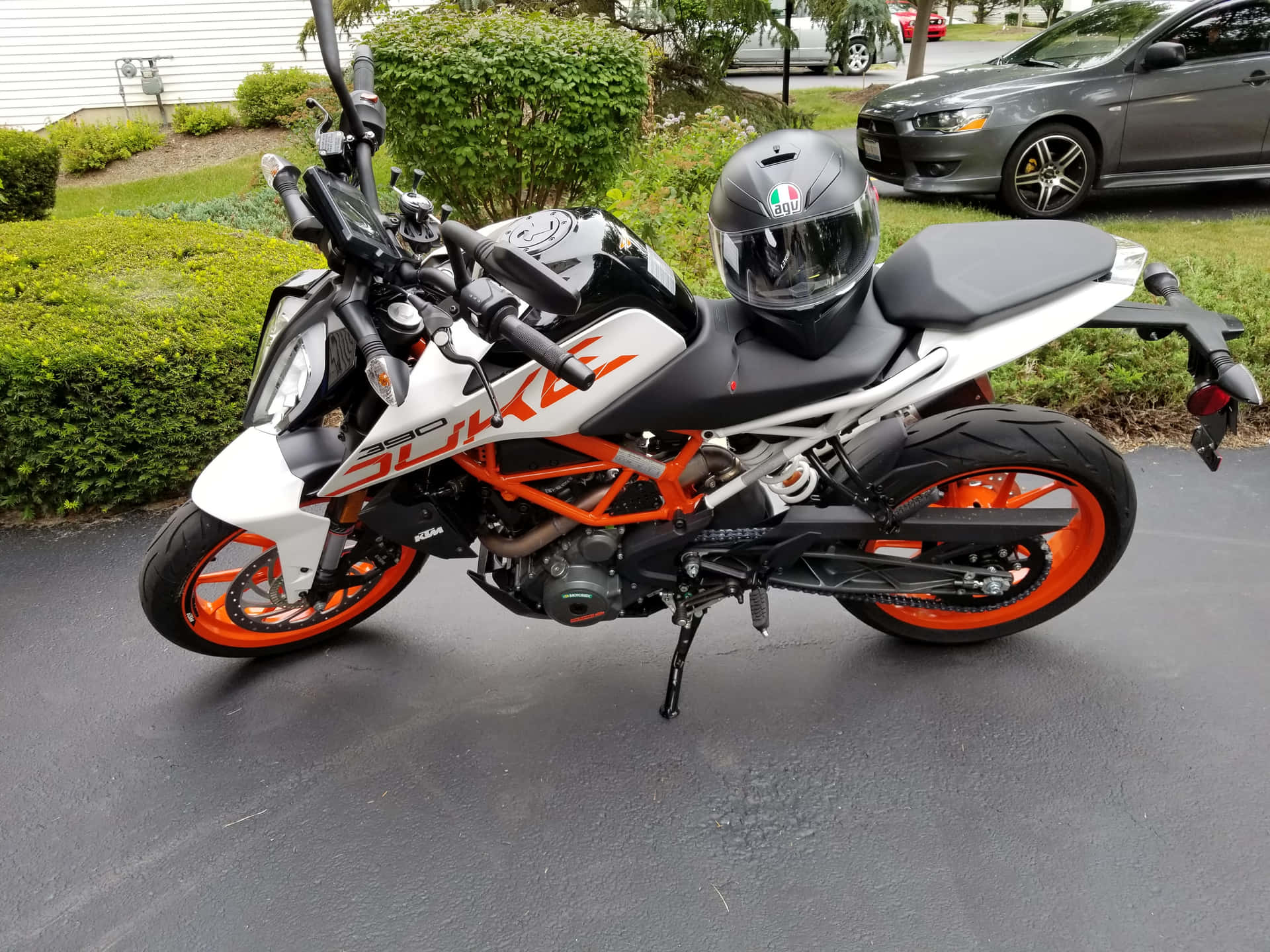  壁紙 — 一輛白色和橙色的KTM 390 Duke摩托車停在濕漉漉的路面上，座位上放著一個安全帽。