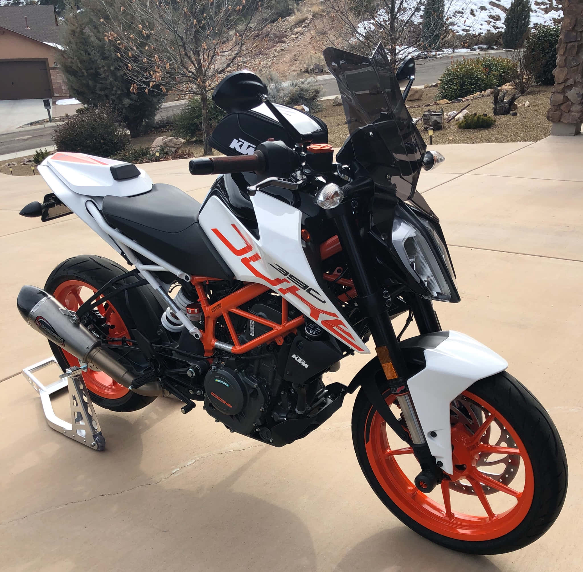 機車 桌布 壁紙 — 一輛白色和橙色的KTM Duke 390摩托車停放在混凝土車道上，背景是白雪覆蓋的山脈和光禿禿的樹木。