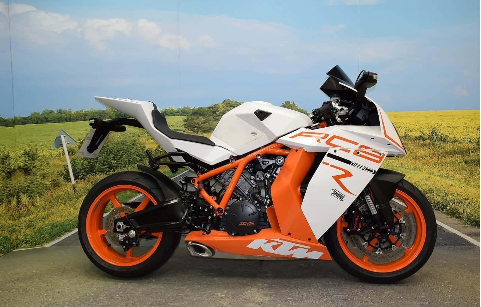 機車 桌布 壁紙 — 一輛白色和橙色的KTM RC390機車停放在鋪砌道路上，旁邊是金色田野，天空蔚藍，白雲點點。