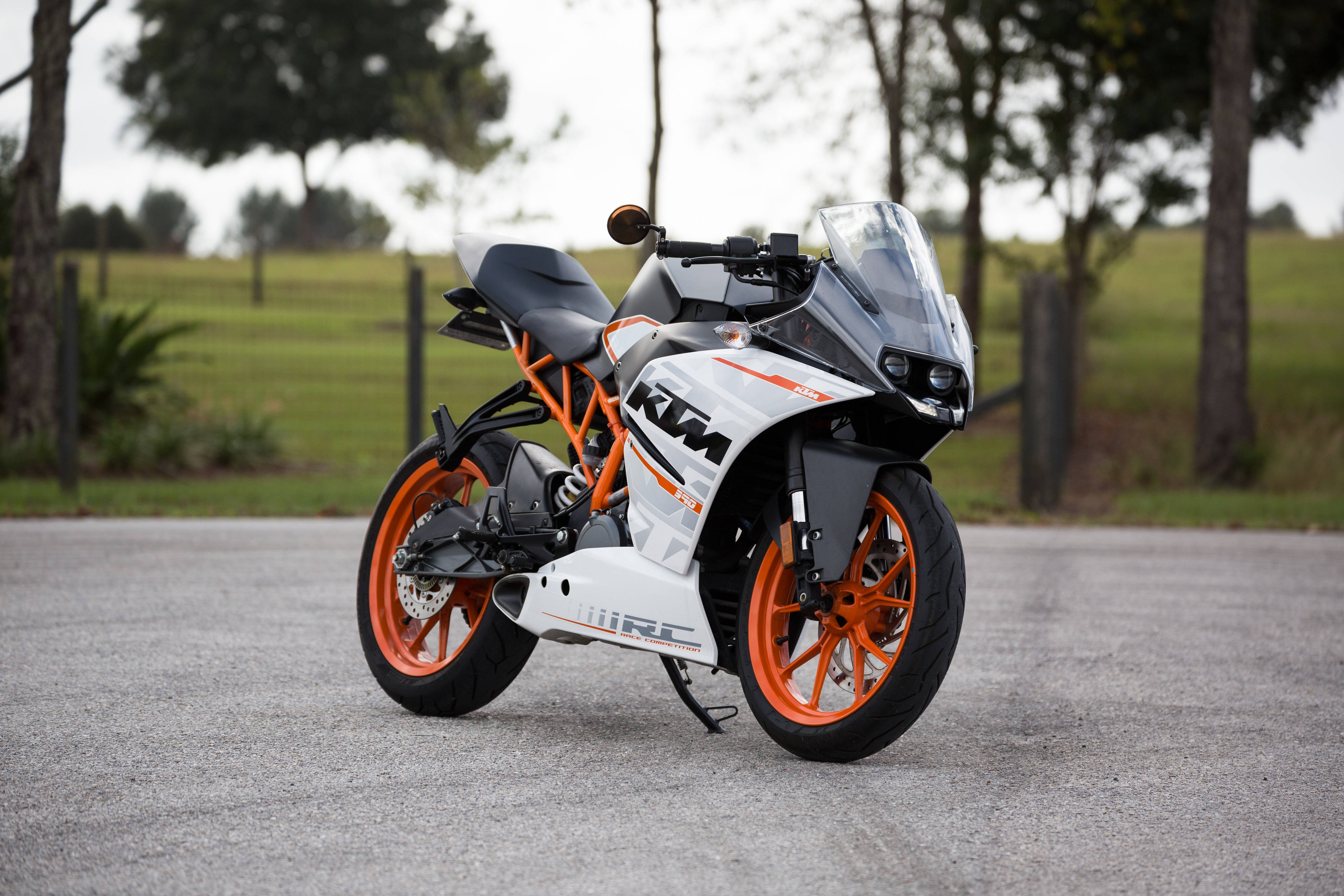 機車 桌布 壁紙 — 一輛白色和橙色的KTM RC摩托車，時尚地停在碎石路上，背景有樹木和草地。