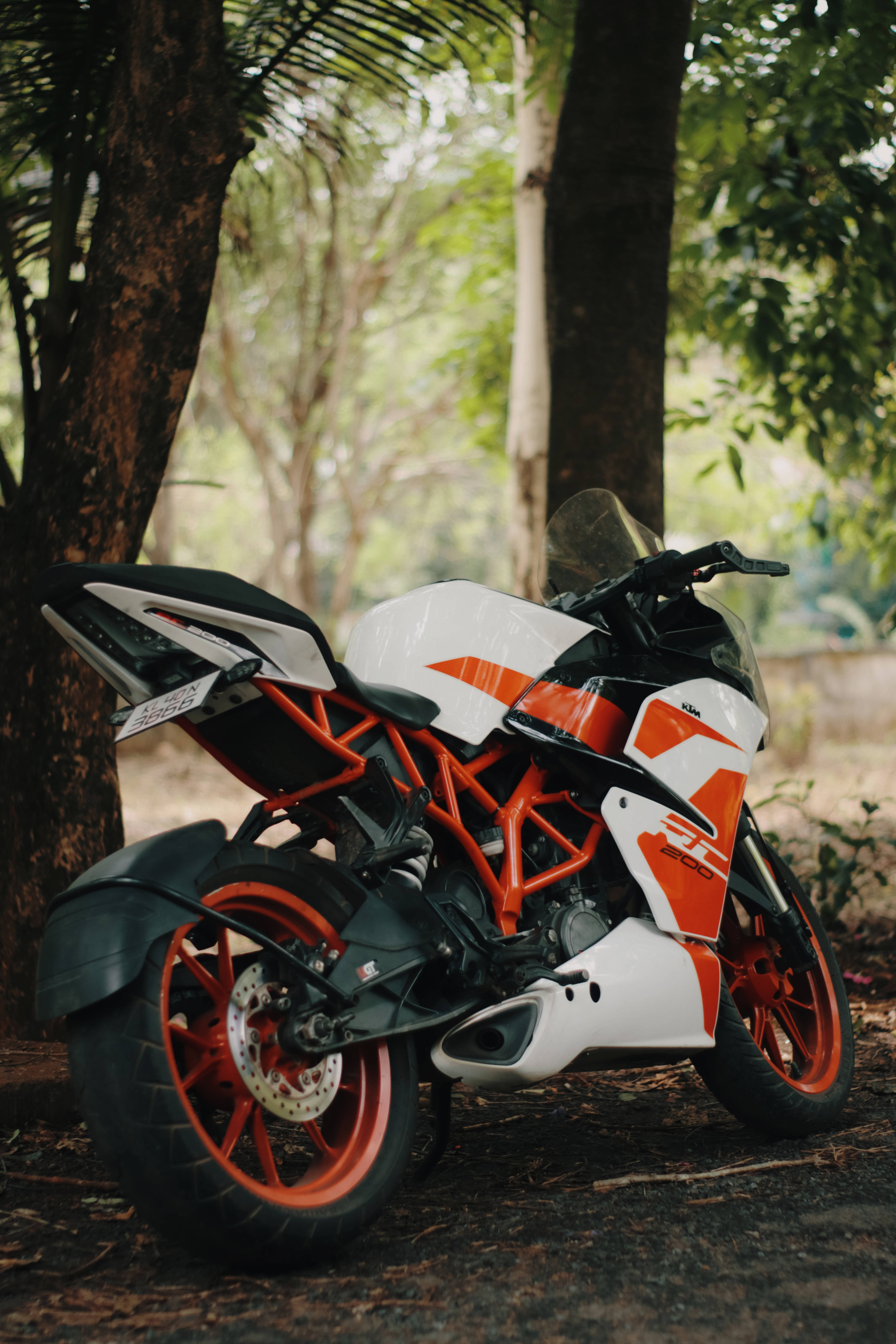 KTM 摩托車 桌布 壁紙 — 一輛白色和橙色的KTM摩托車停放在森林中樹葉茂密的樹下，陽光斑駁。