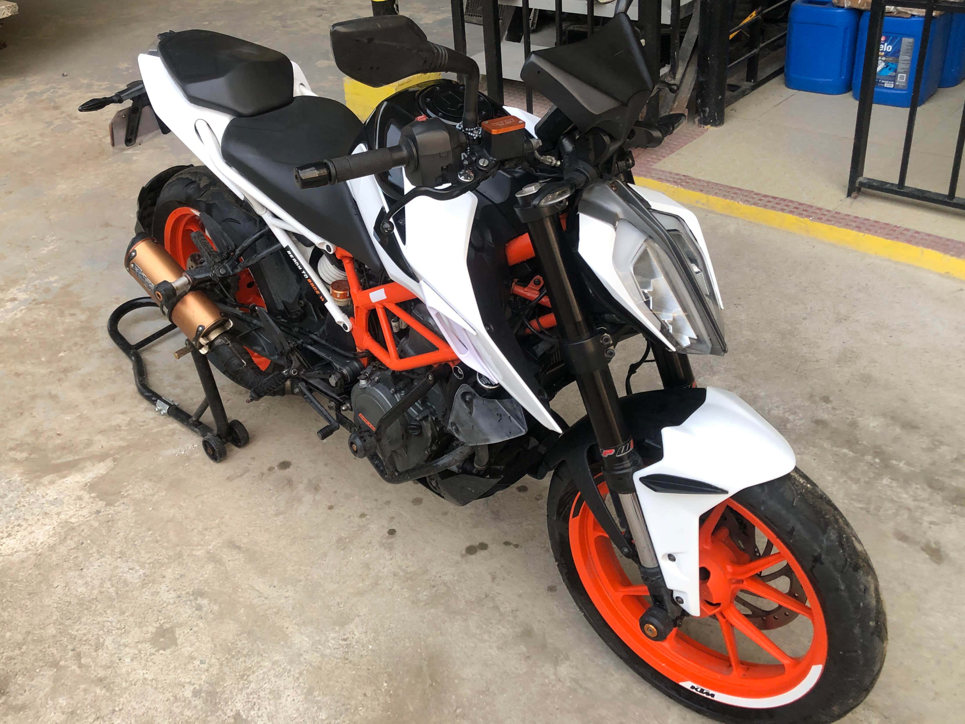 機車 桌布 壁紙 — 一輛白色和橙色的KTM摩托車停放在車庫的混凝土地板上，背景有藍色桶子。