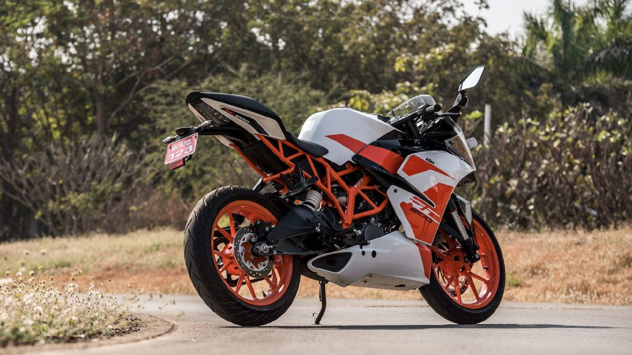 KTM RC 200 桌布 壁紙 — 一輛白色和橙色的KTM機車停放在鋪砌的道路上，背景有乾草和樹木。