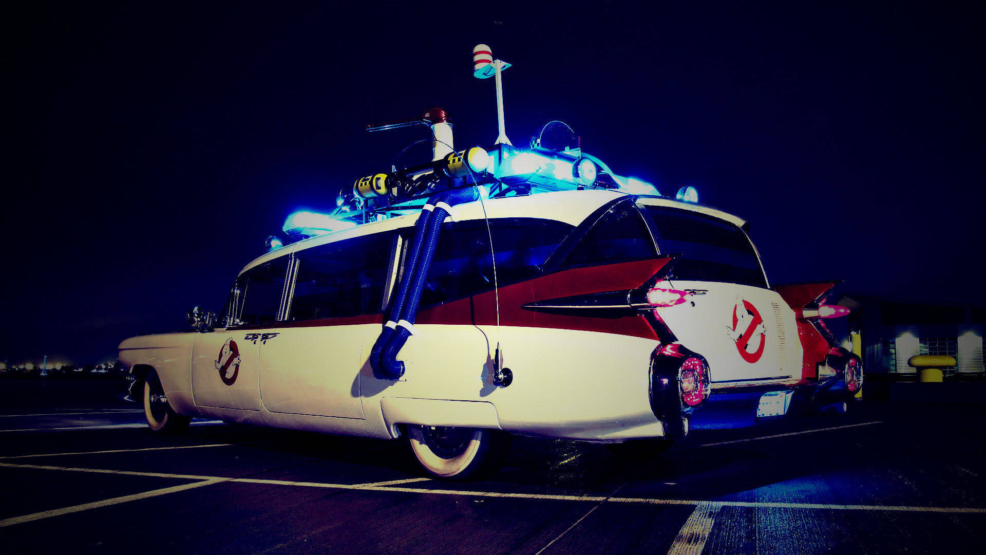 魔鬼剋星 桌布 壁紙 — 一輛白色和紅色的Ghostbusters Ecto-1汽車，帶有發光的藍色燈光，夜間停在黑暗的停車場。