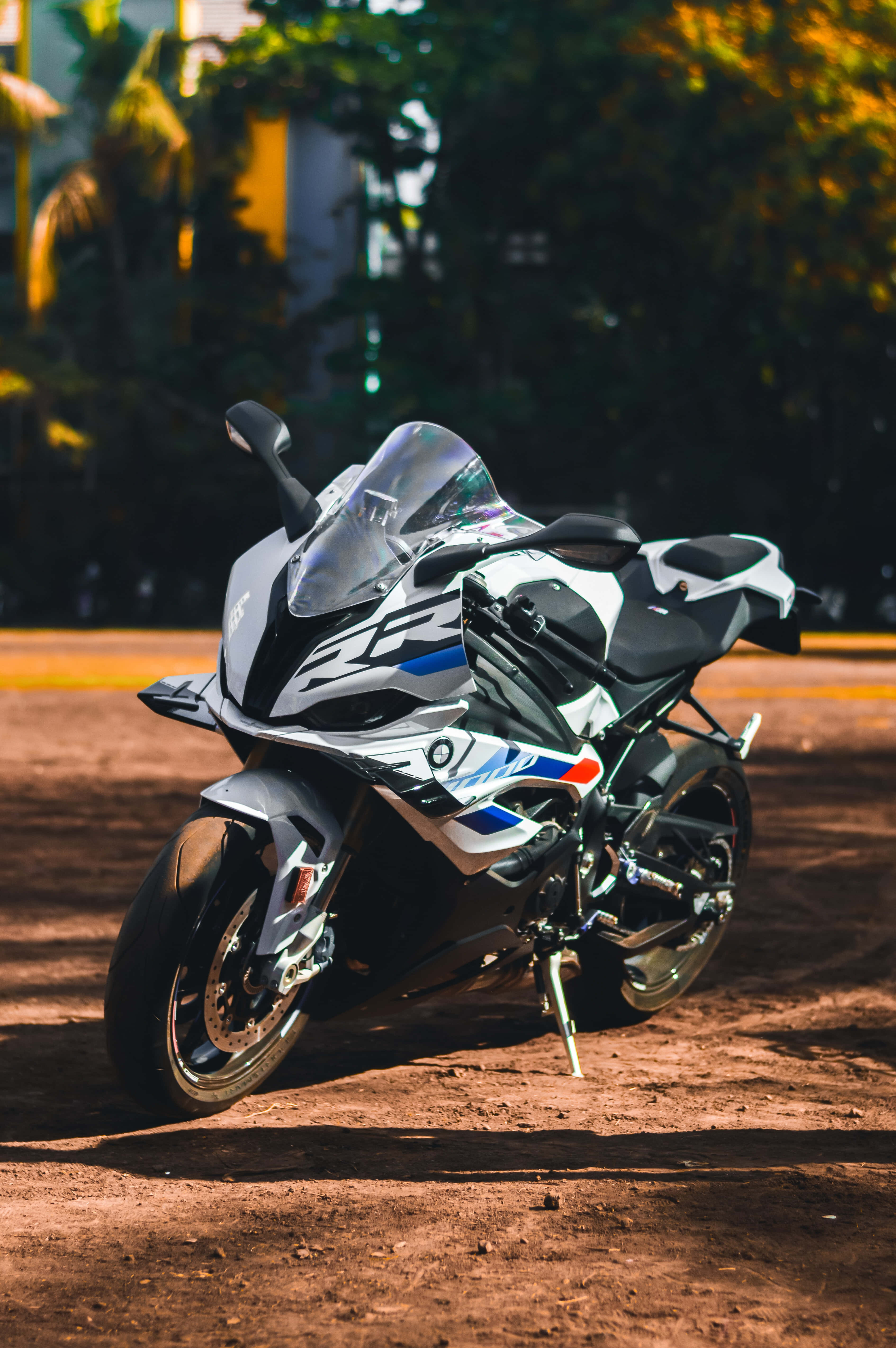 Superbike 桌布 壁紙 — 一輛白色和藍色的運動機車停泊在泥土上，陽光斑駁，背景有綠色樹葉。