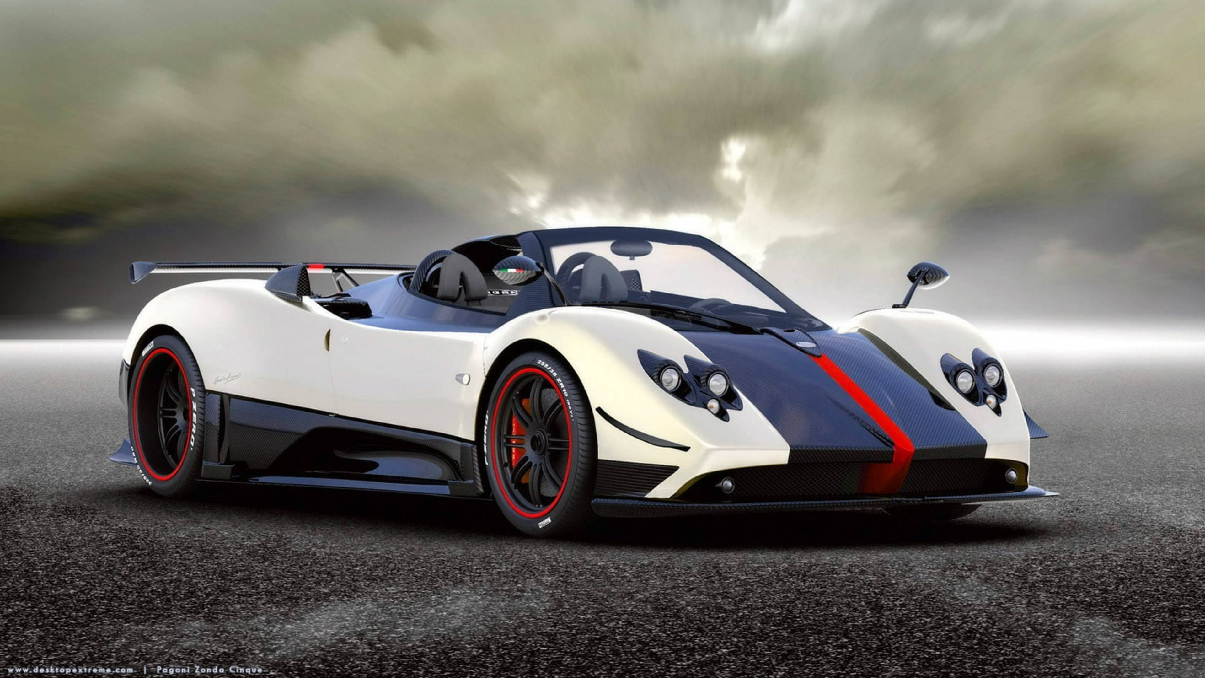 Pagani 桌布 壁紙 — 一輛白色和黑色的帕加尼Zonda Cinque敞篷跑車，帶有紅色點綴，在戲劇性的暴風雨天空下，停在潮濕的瀝青路面上。