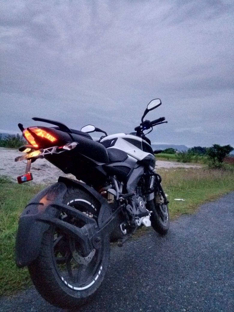  壁紙 — 一輛白色和黑色的摩托車，帶有發光的紅色尾燈，停泊在黃昏時分多雲天空下的碎石路上。