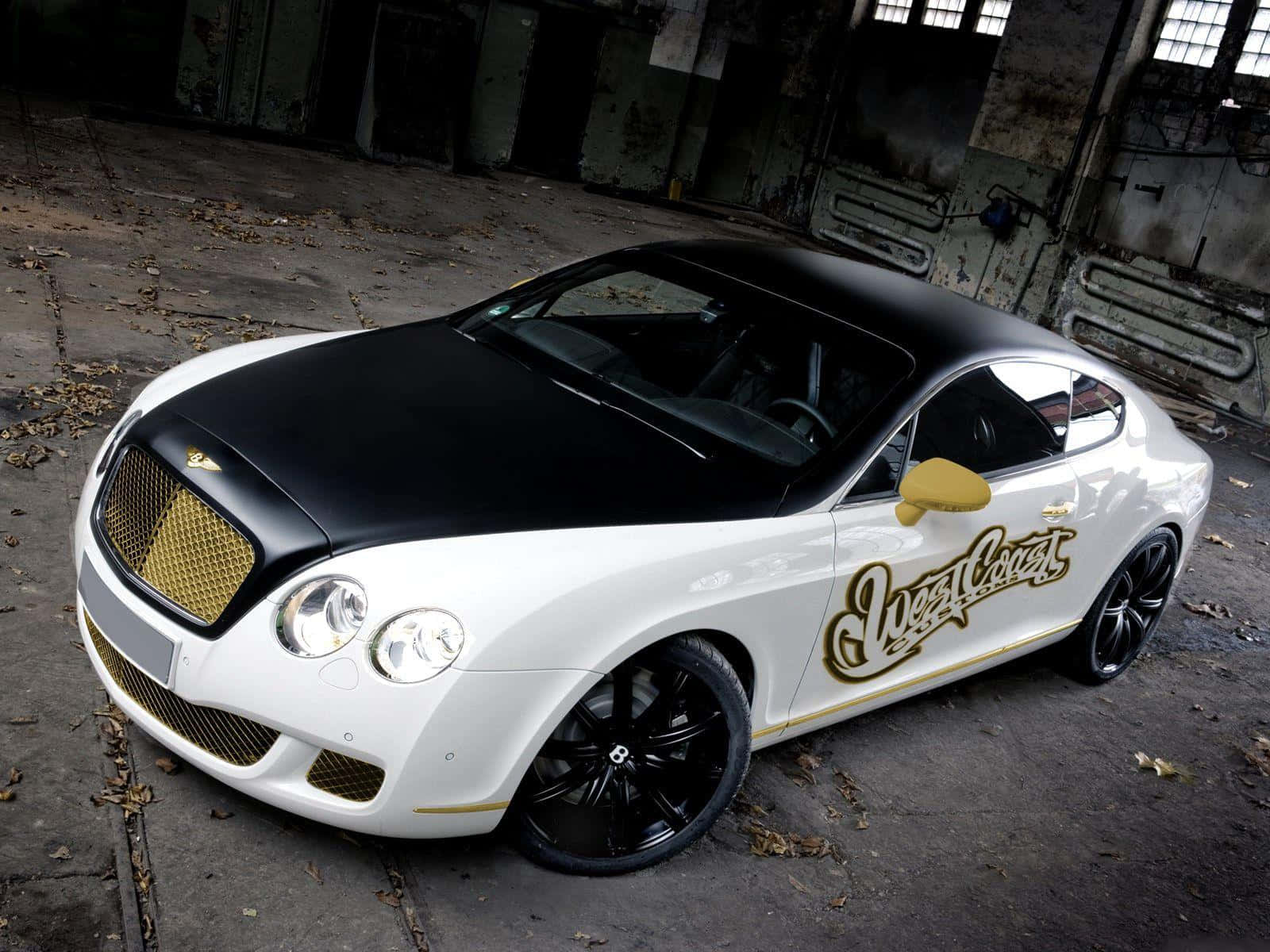 Modified Car 桌布 壁紙 — 一輛白色和黑色的賓利 Continental GT，帶有金色 'West Coast' 字樣，停放在一個骯髒的廢棄倉庫中。