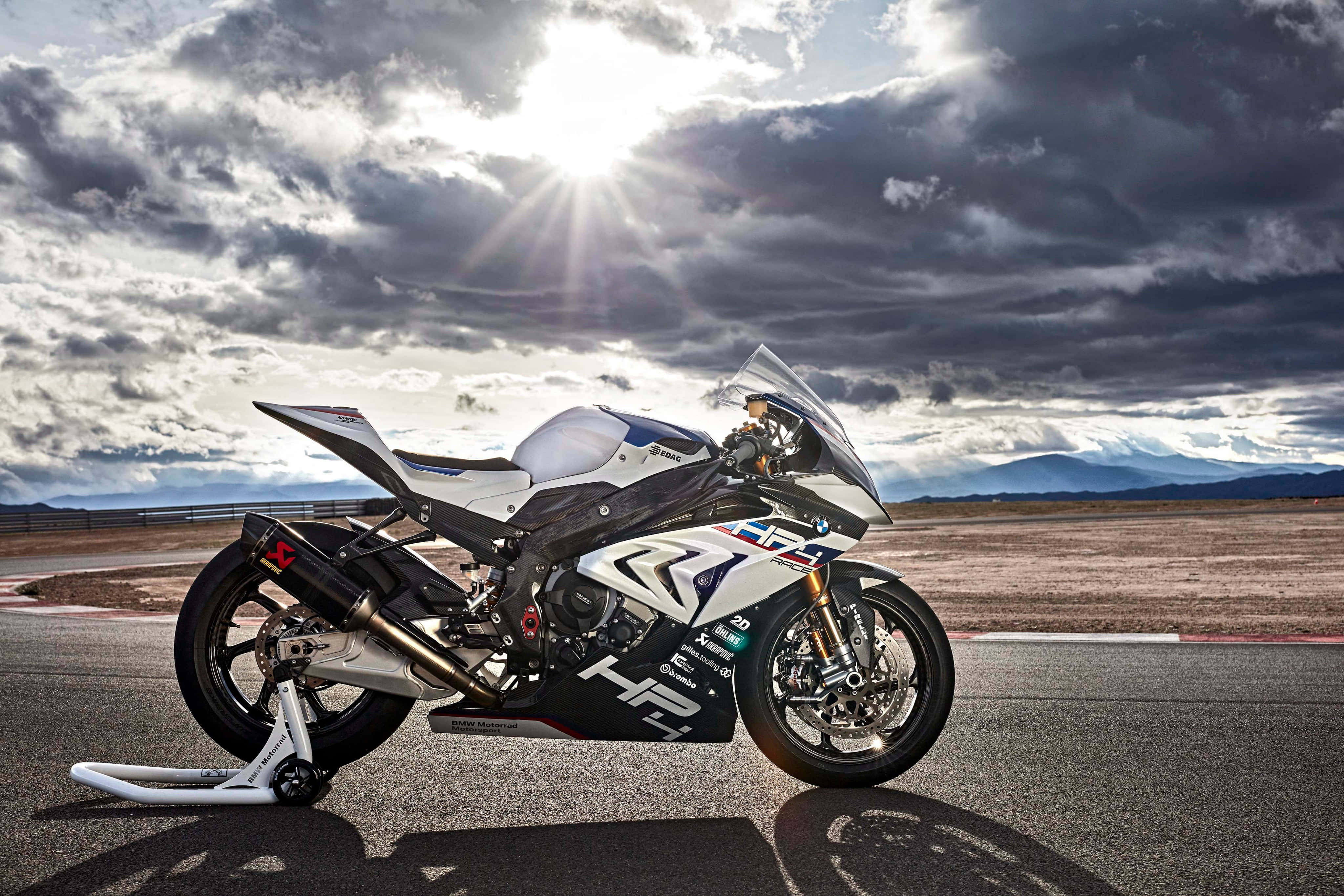 Superbike 桌布 壁紙 — 一輛白色和黑色的賽車摩托車在賽道上，背景是暴風雲層中戲劇性的陽光穿透。