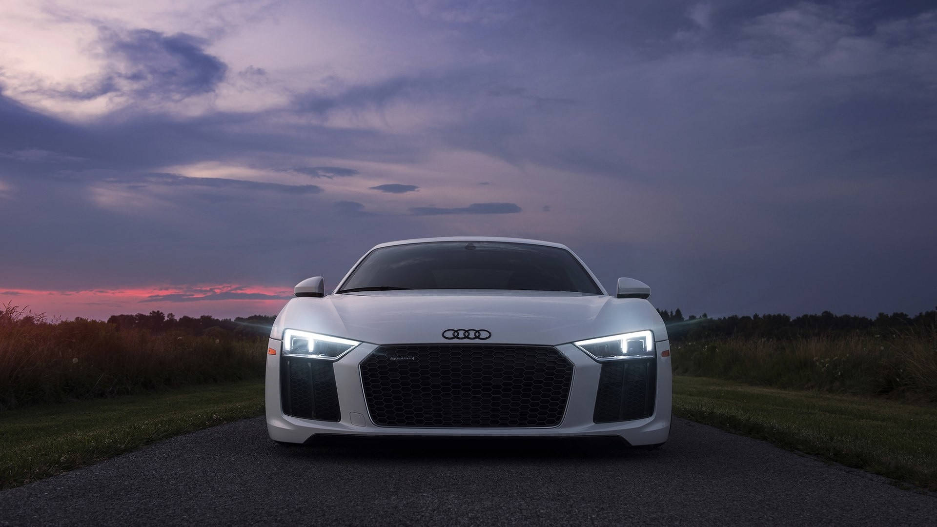R8 桌布 壁紙 — 一輛白色奧迪R8跑車在戲劇性的暮色天空下，在鄉村道路上亮著車頭燈向前行駛。