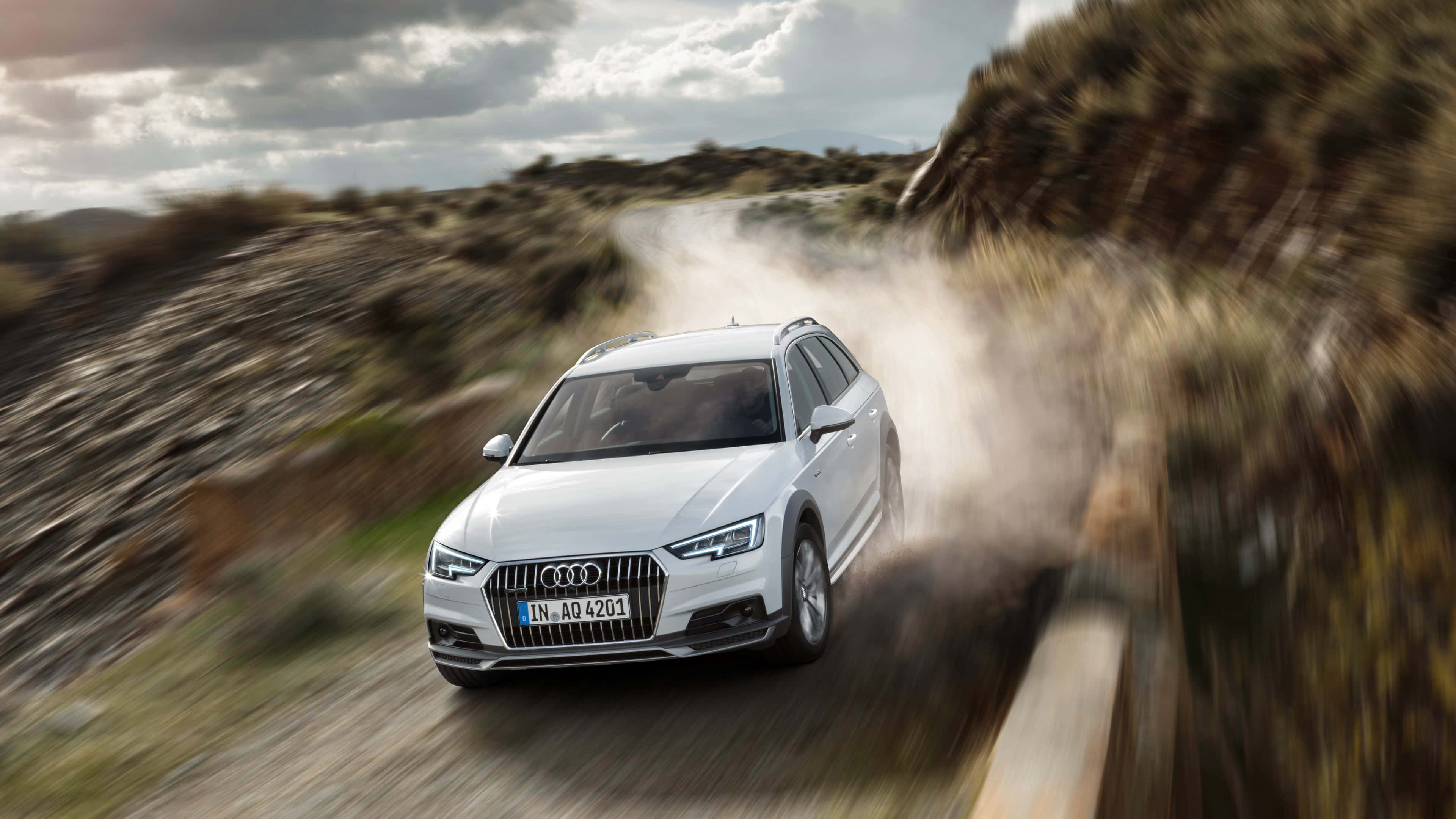 Audi A4 桌布 壁紙 — 一輛白色奧迪SUV在多雲的天空下，沿著塵土飛揚的山路高速行駛，揚起滾滾塵土。