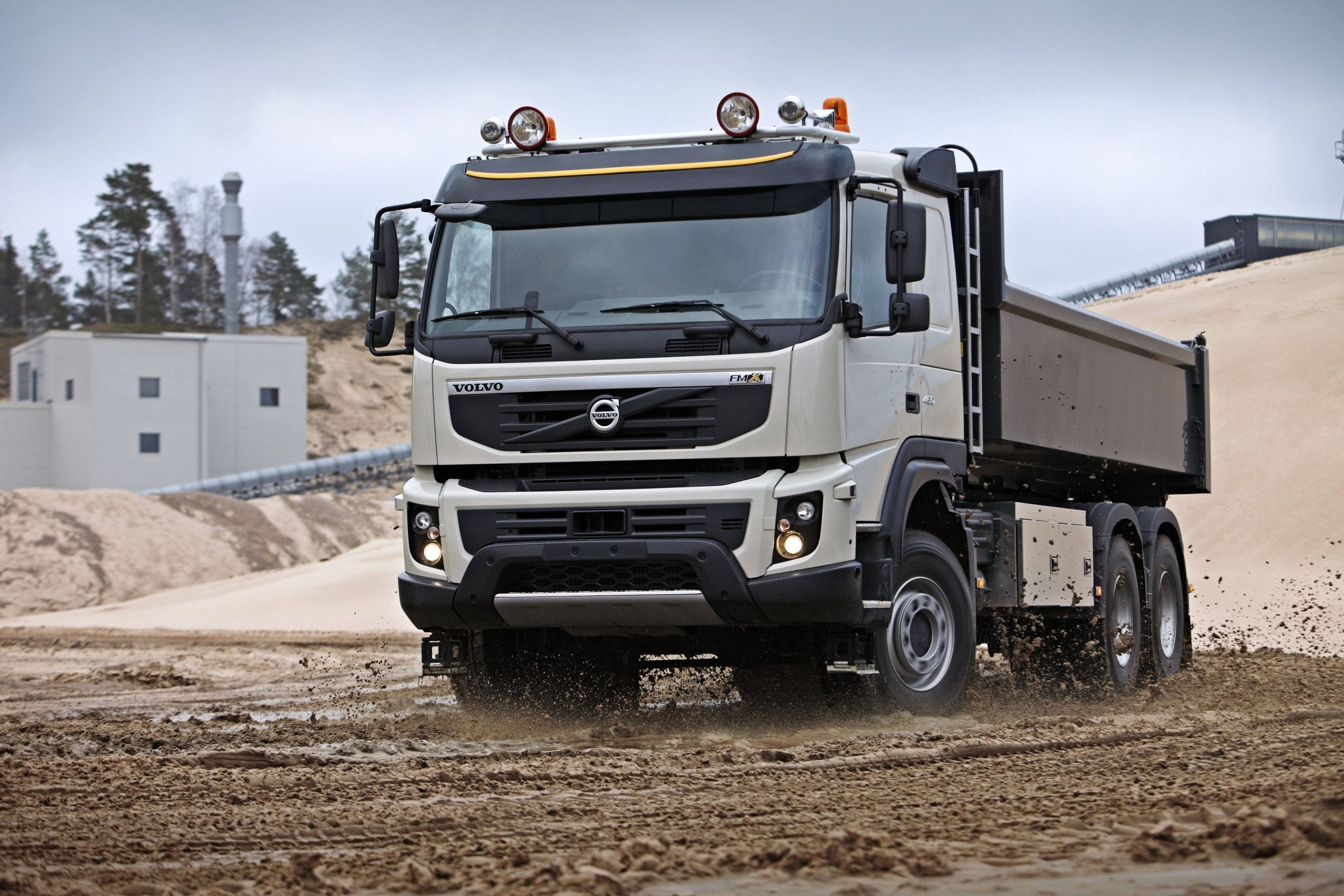 Cool Truck 桌布 壁紙 — 一輛白色富豪自卸車在建築工地的泥濘地形上行駛，在陰天揚起泥土。