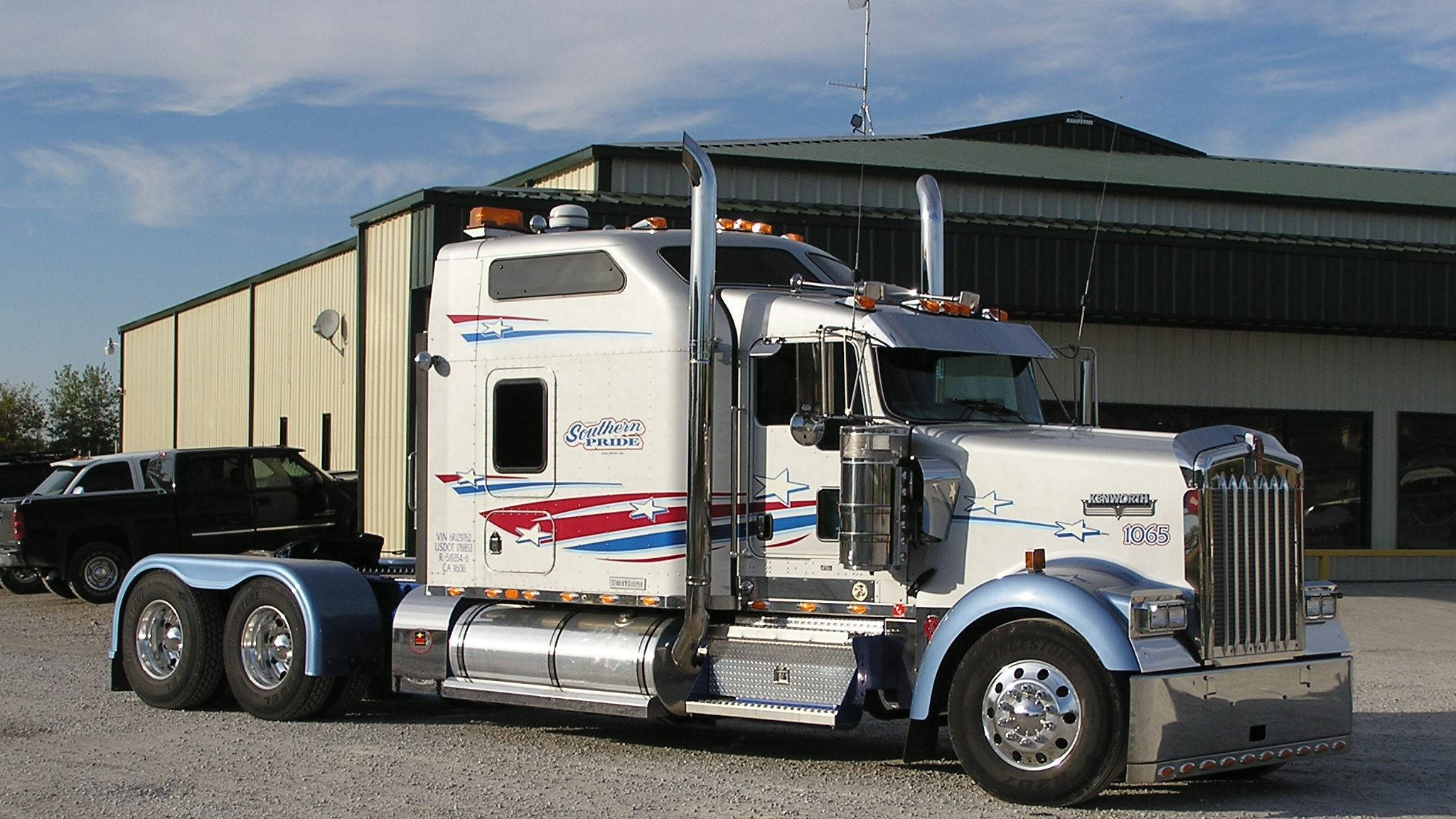 Kenworth 桌布 壁紙 — 一輛白色彼得標半掛卡車，帶有紅藍星星貼花和「Southern Pride」字樣，停在倉庫前，天空部分多雲。