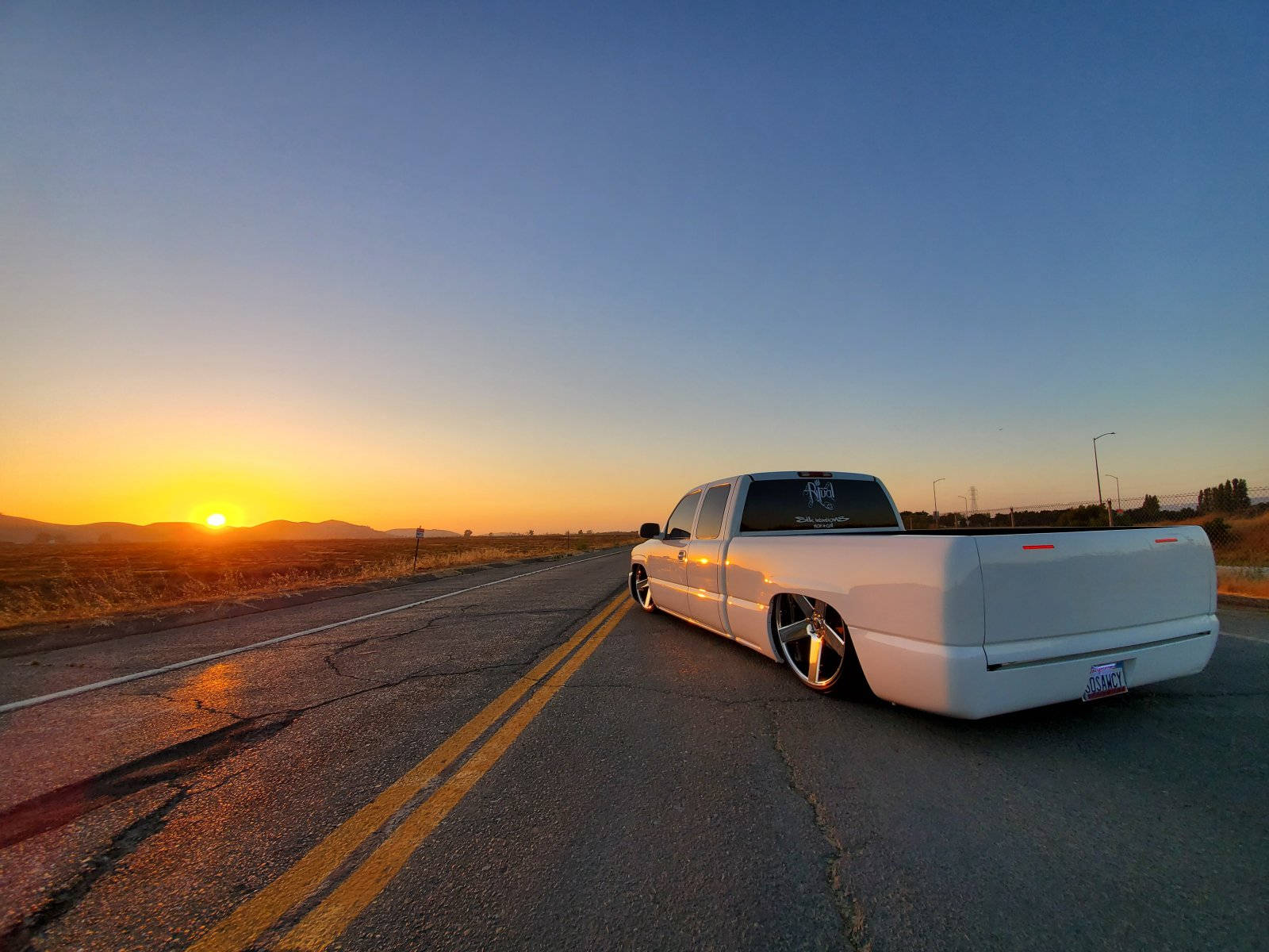 Trucks 桌布 壁紙 — 一輛白色改裝低趴皮卡車停在沙漠公路旁，夕陽金色光芒投下長長的影子。