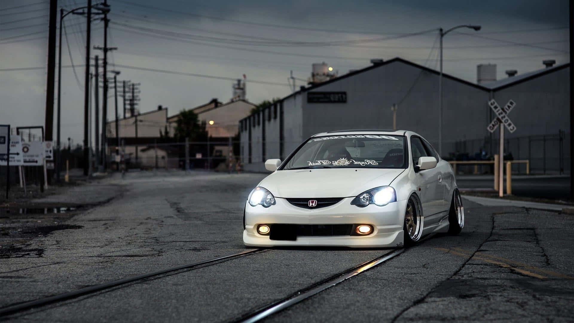Acura Integra 桌布 壁紙 — 一輛白色改裝本田思域在黃昏時低趴於鐵軌上，閃爍的車頭燈照亮了粗糙的工業街道。