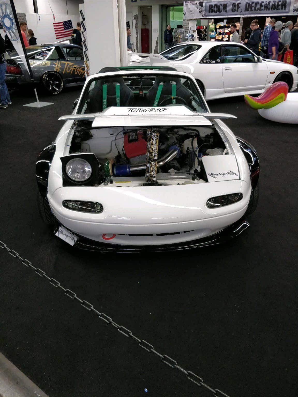 跑車 桌布 壁紙 — 一輛白色改裝的馬自達MX-5，引擎蓋打開展示定制引擎，在室內車展中展出，背景有人群和其他車輛。