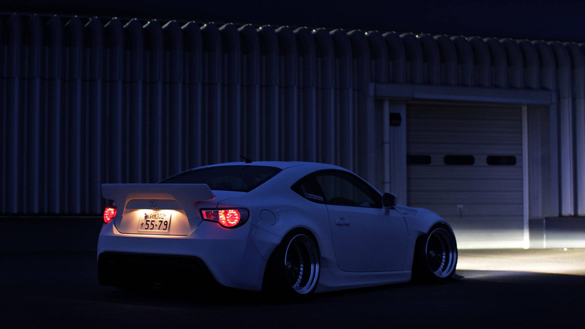 白色改裝跑車，帶有發光尾燈，夜間停放在倉庫旁邊。 — Toyota Supra Mk4 壁紙