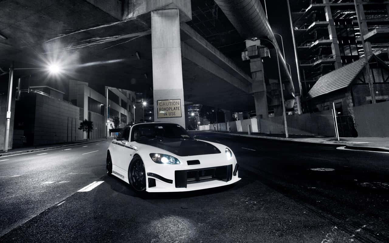 Honda S2000 桌布 壁紙 — 一輛白色改裝跑車，車頭燈發光，夜晚停在混凝土天橋下，街燈照明強烈。