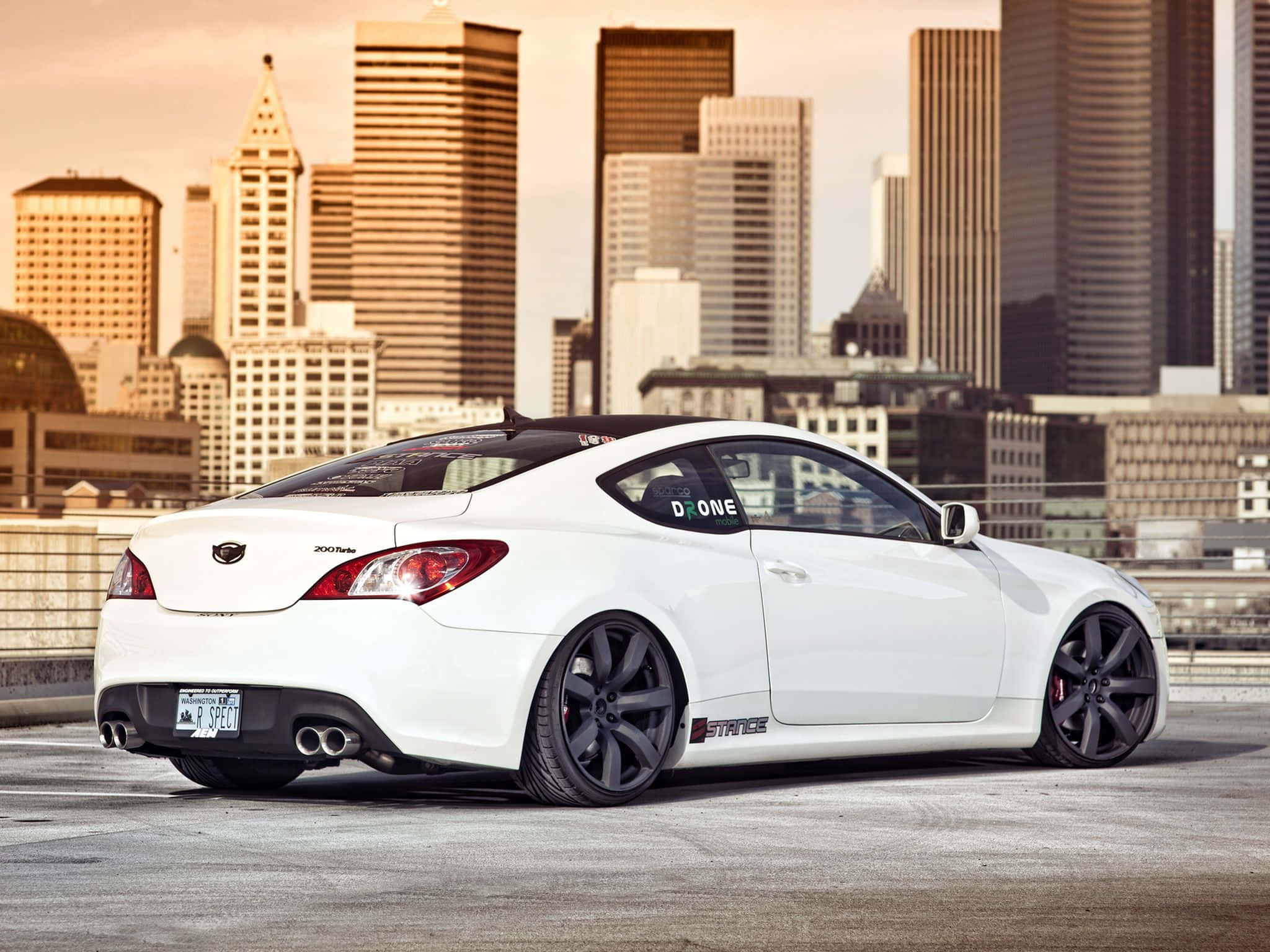 Hyundai Genesis 桌布 壁紙 — 一輛白色改裝跑車配黑色輪圈，停在天台上，俯瞰黃金時段的城市天際線。