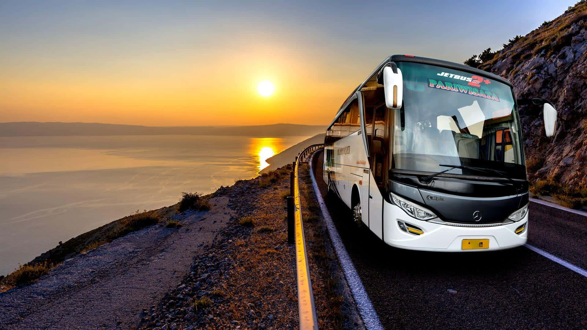 Bus 桌布 壁紙 — 一輛白色旅遊巴士在日落時分沿著海岸道路行駛，金色的光芒反射在海面上。