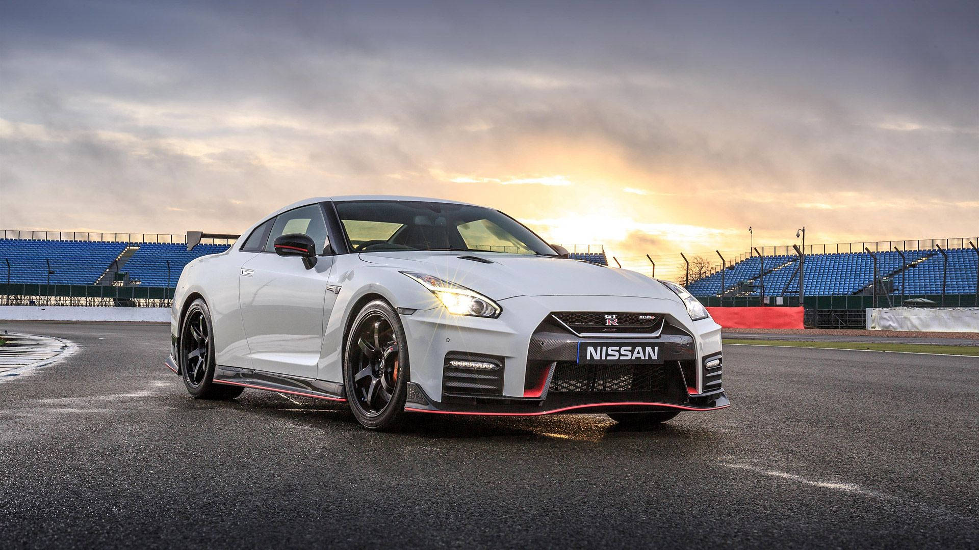 Nissan 桌布 壁紙 — 一輛白色日產GT-R跑車帶有紅色點綴，在日落時分停在賽車場上，後面是空無一人的藍色看台。