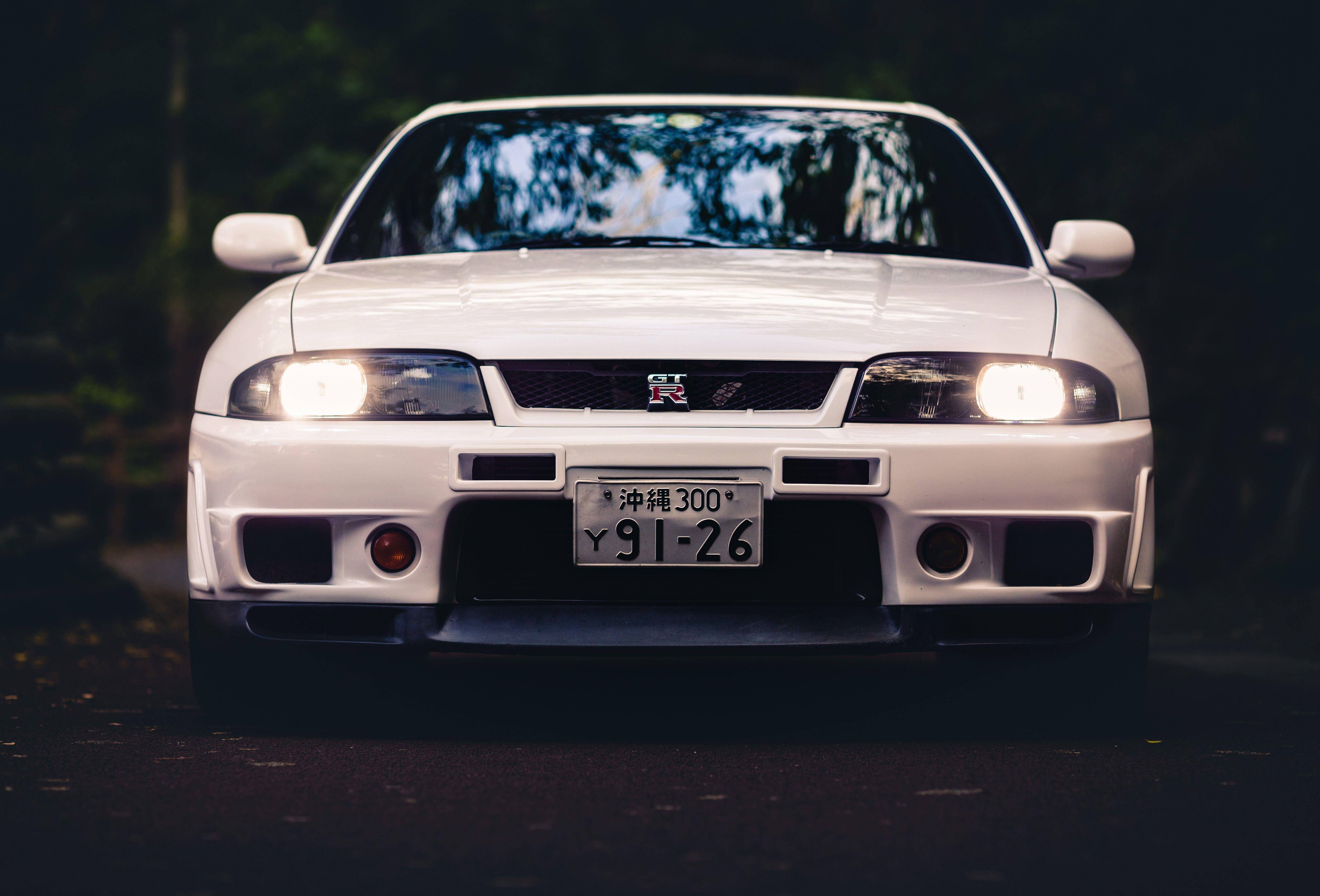 Gtr 桌布 壁紙 — 一輛白色日產Skyline GT-R在暮色下的黑暗森林道路上，亮著車頭燈向前。