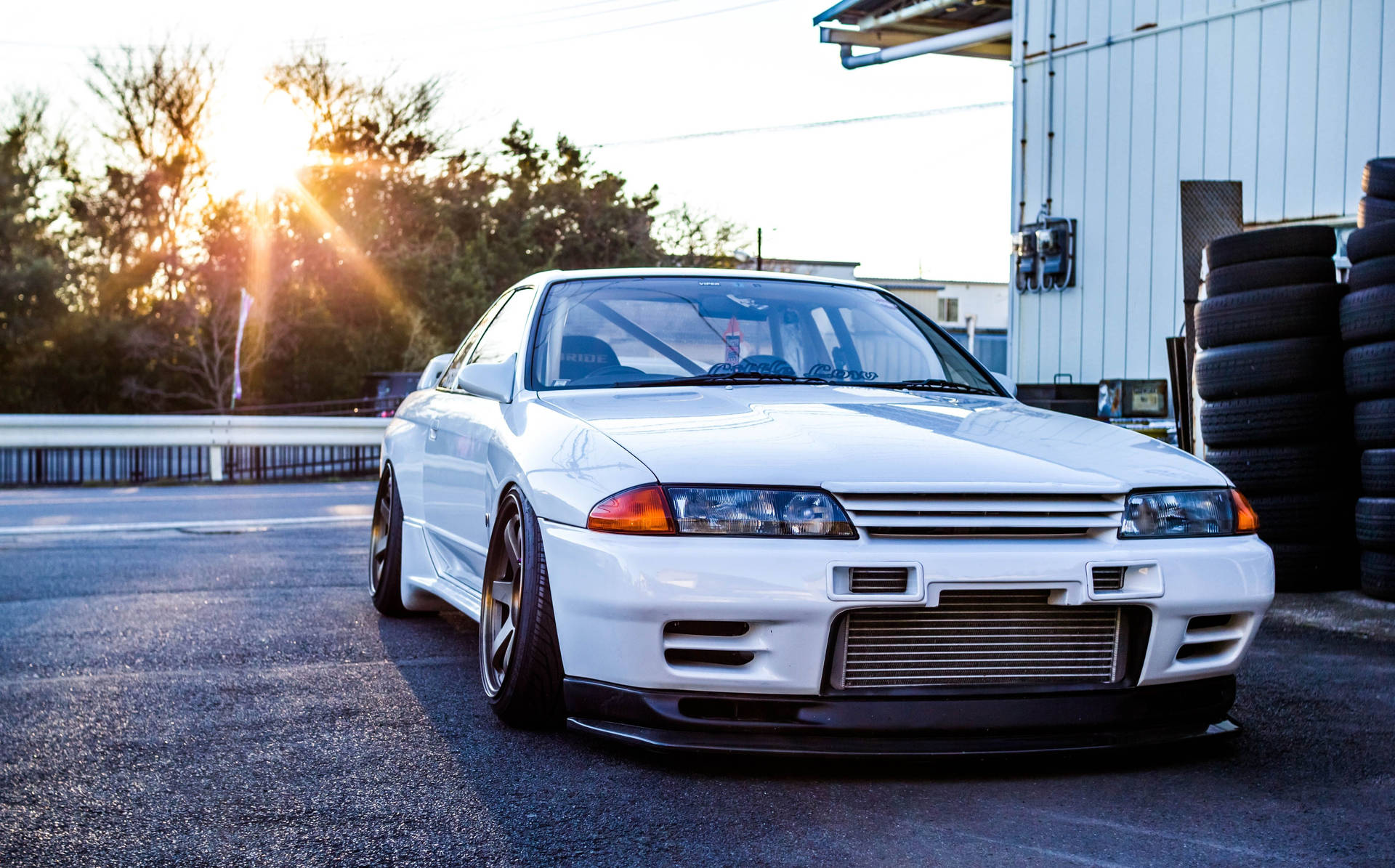 白色日產Skyline R32在日落時停放在輪胎堆附近。 — 4K Jdm 壁紙