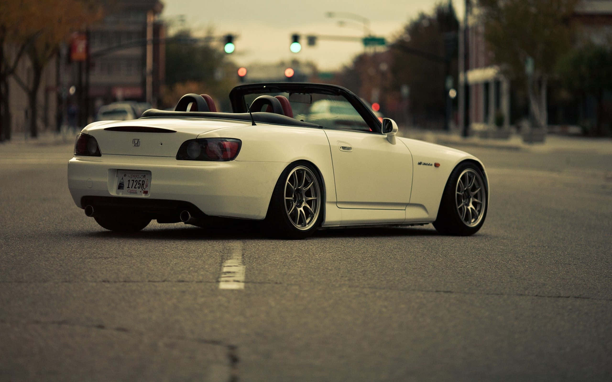 Honda S2000 桌布 壁紙 — 一輛白色本田S2000敞篷跑車在黃昏時停泊在城市街道上，背景有交通號誌亮起。