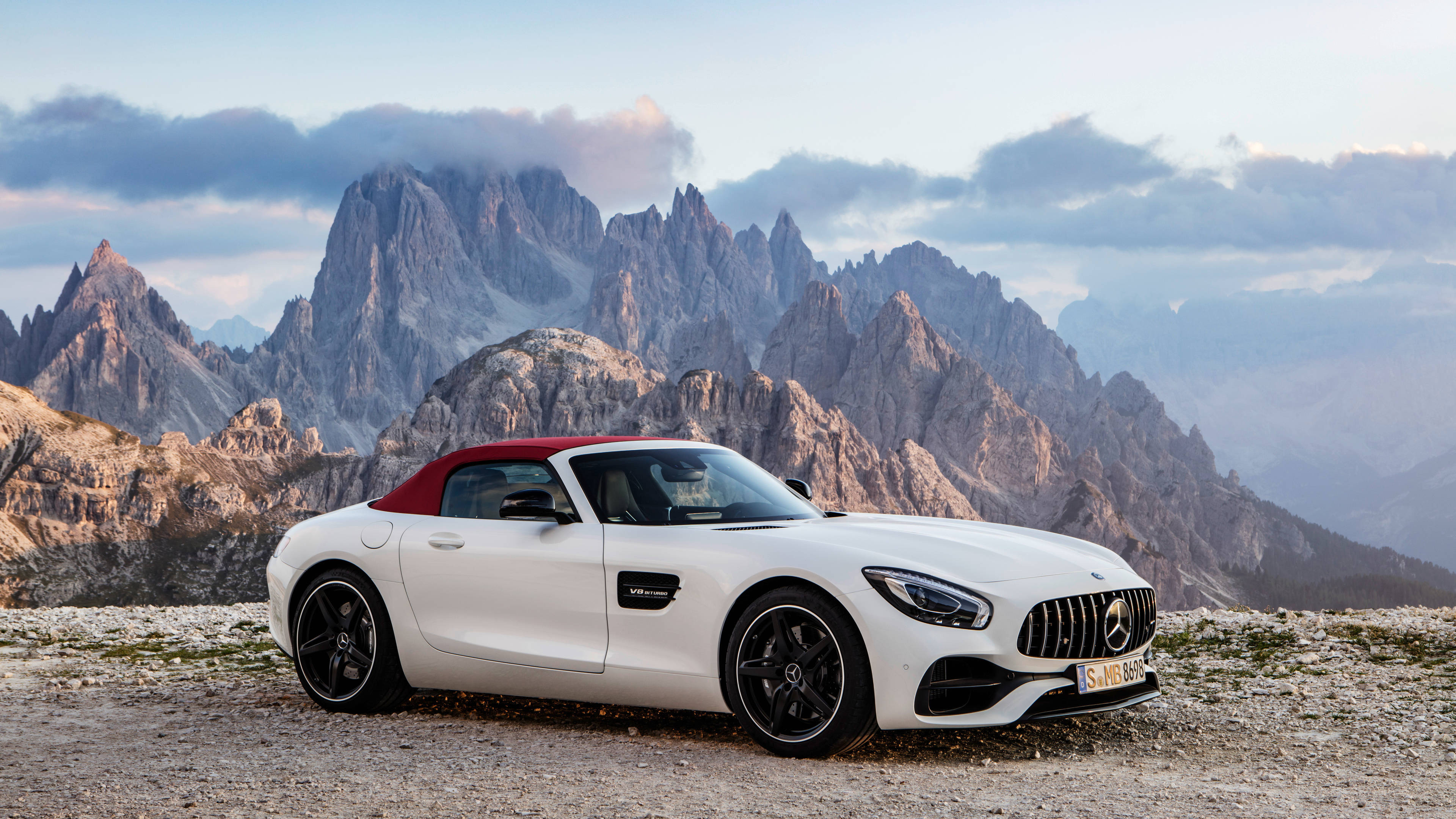 4K 奔馳壁紙 桌布 壁紙 — 一輛白色梅賽德斯-AMG GT Roadster，紅色軟頂，停泊在多岩石的山口，背景是鋸齒狀山峰，天空多雲。