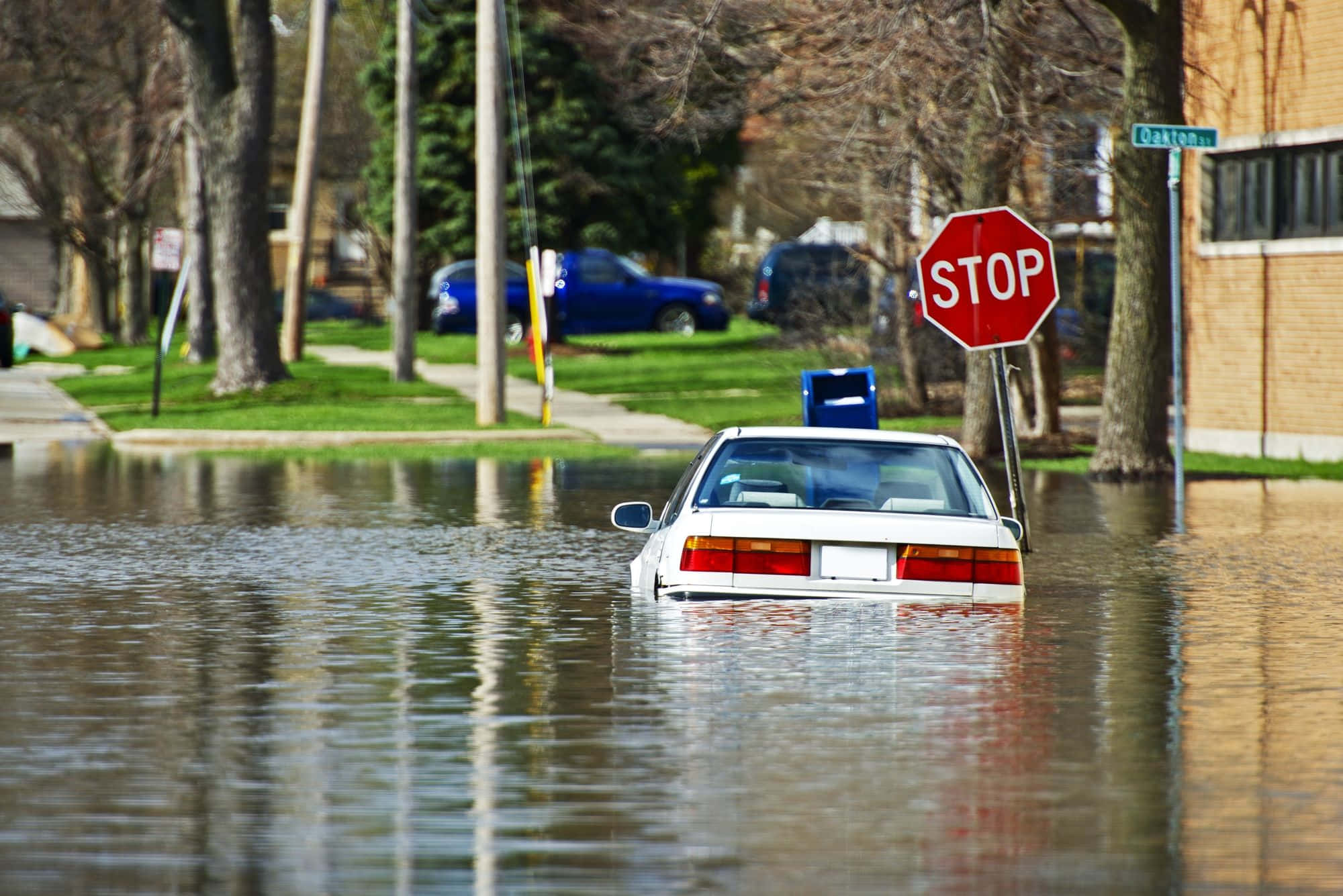 Flood 桌布 壁紙 — 一輛白色汽車淹沒在住宅街道的洪水中，附近有一個停車標誌。