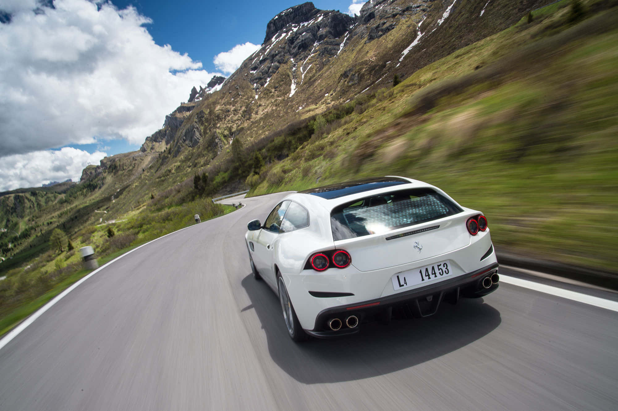 Ferrari Gtc4lusso 桌布 壁紙 — 一輛白色法拉利在蜿蜒的山路上奔馳，兩旁是白雪覆蓋的山峰和翠綠的山坡，頭頂是明亮的藍天。