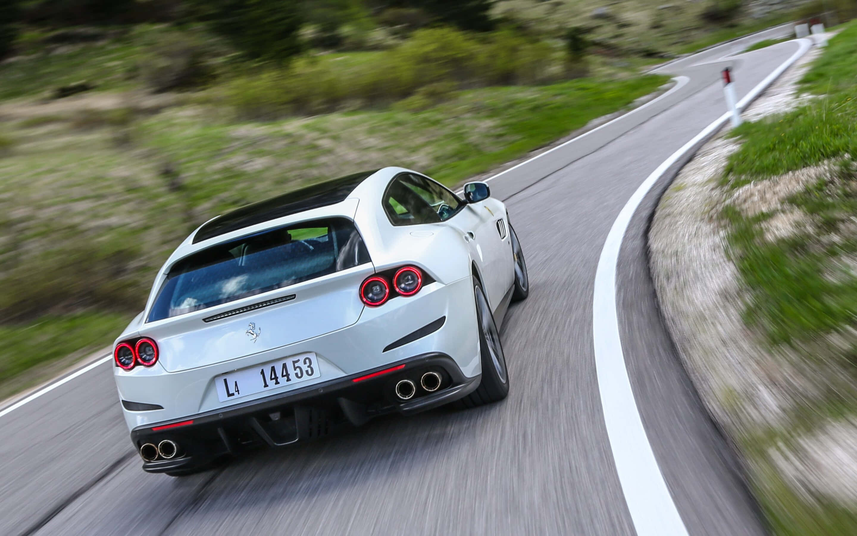 Ferrari Gtc4lusso 桌布 壁紙 — 一輛白色法拉利在蜿蜒的山路上高速行駛，周圍有模糊的綠色植物和白色標線。