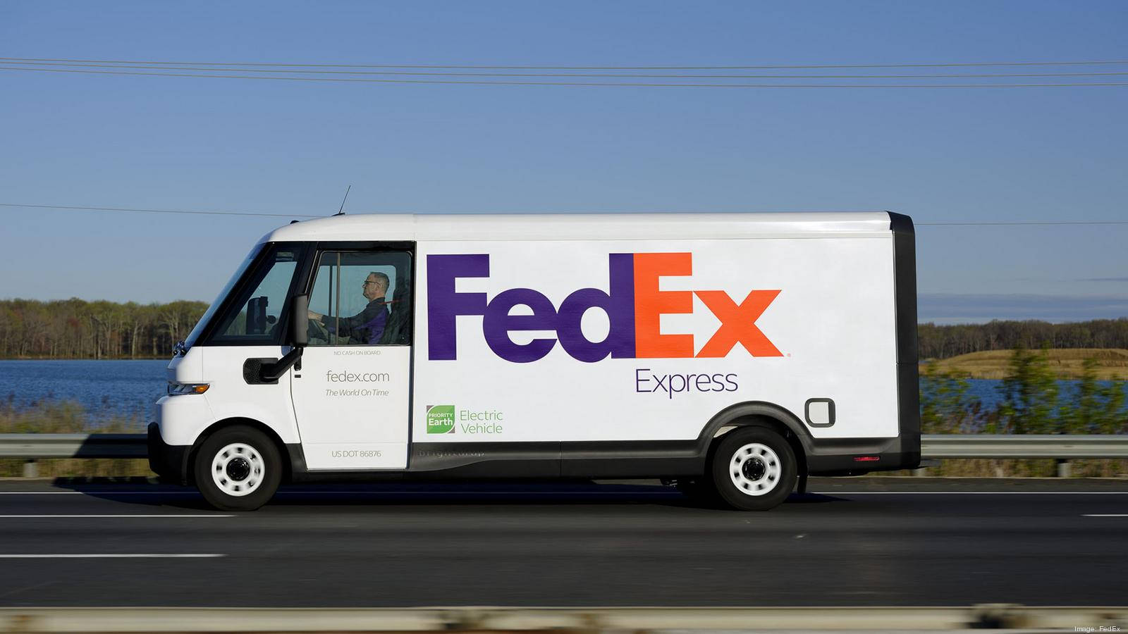 聯邦快遞 桌布 壁紙 — 一輛白色的FedEx Express電動送貨車在晴朗藍天下，沿著平靜湖泊旁的高速公路行駛。