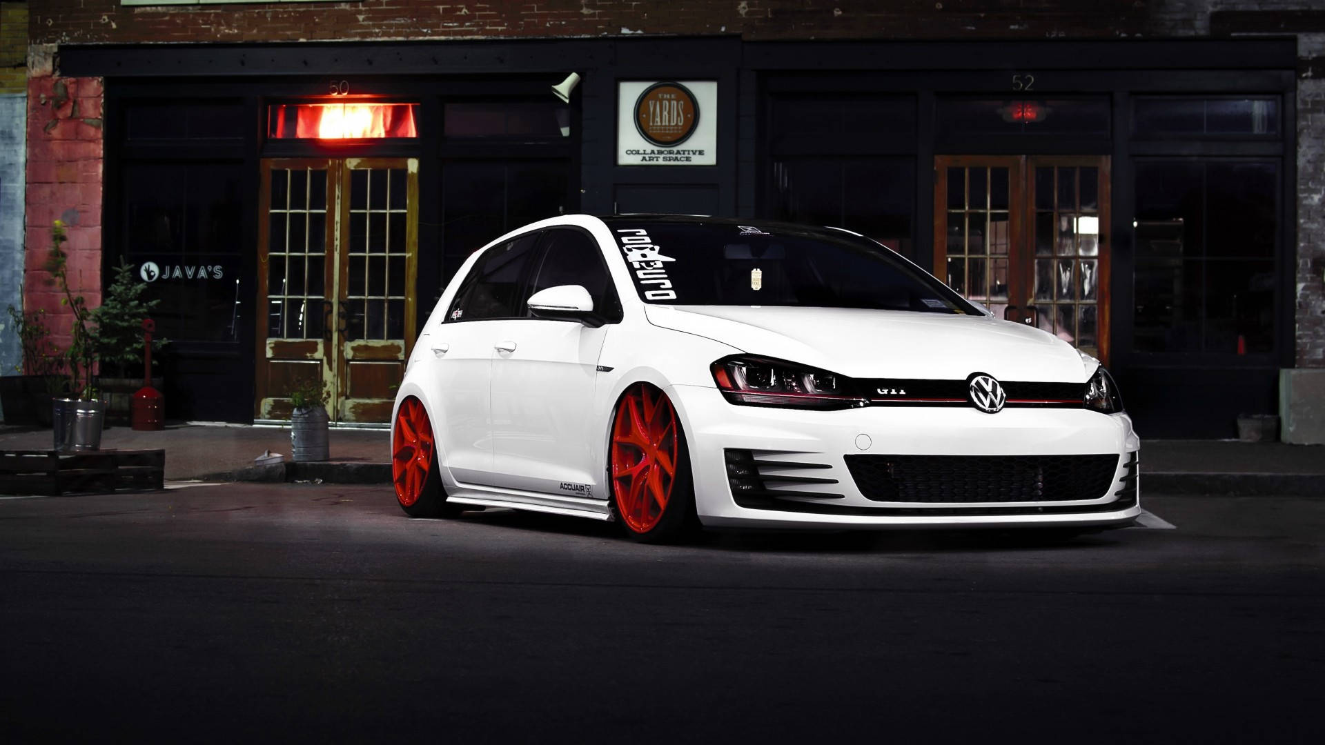 Gti 桌布 壁紙 — 一輛白色福斯Golf配以大膽紅色輪圈，夜間停放在帶有發光招牌的磚造建築前。