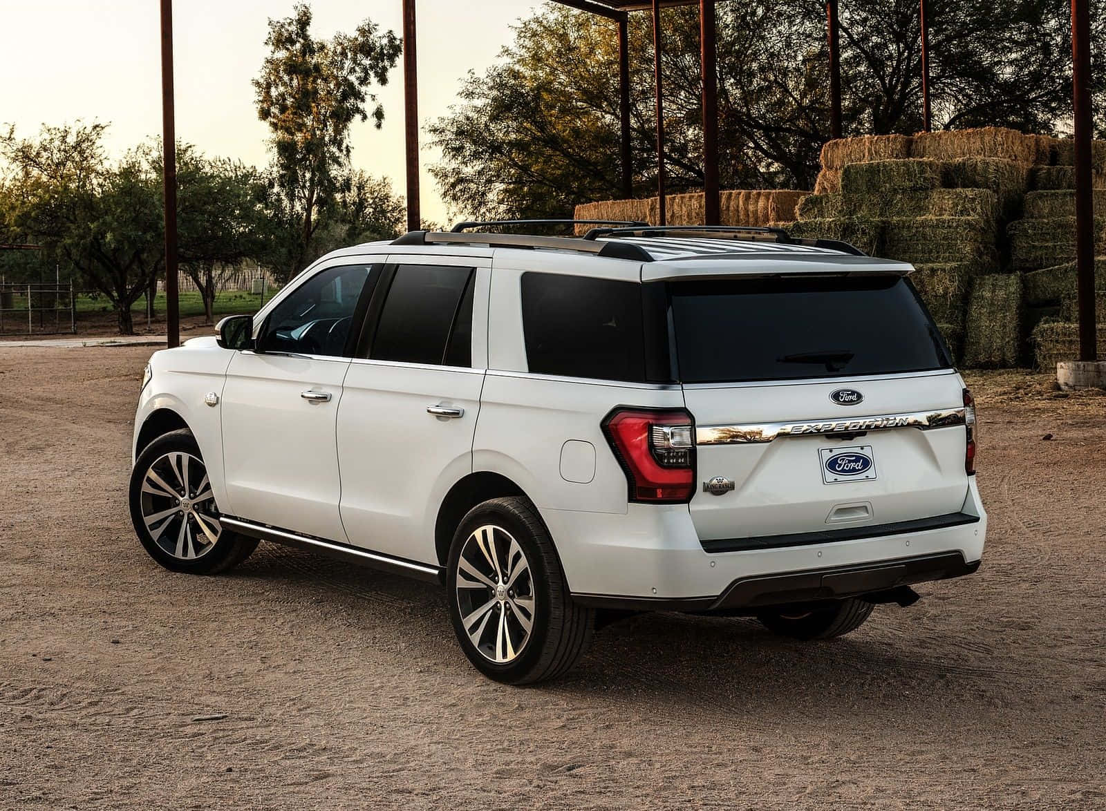Ford Expedition 桌布 壁紙 — 一輛白色福特Explorer SUV停泊在泥土上，旁邊是堆疊的乾草捆，沐浴在溫暖的金色時光中。