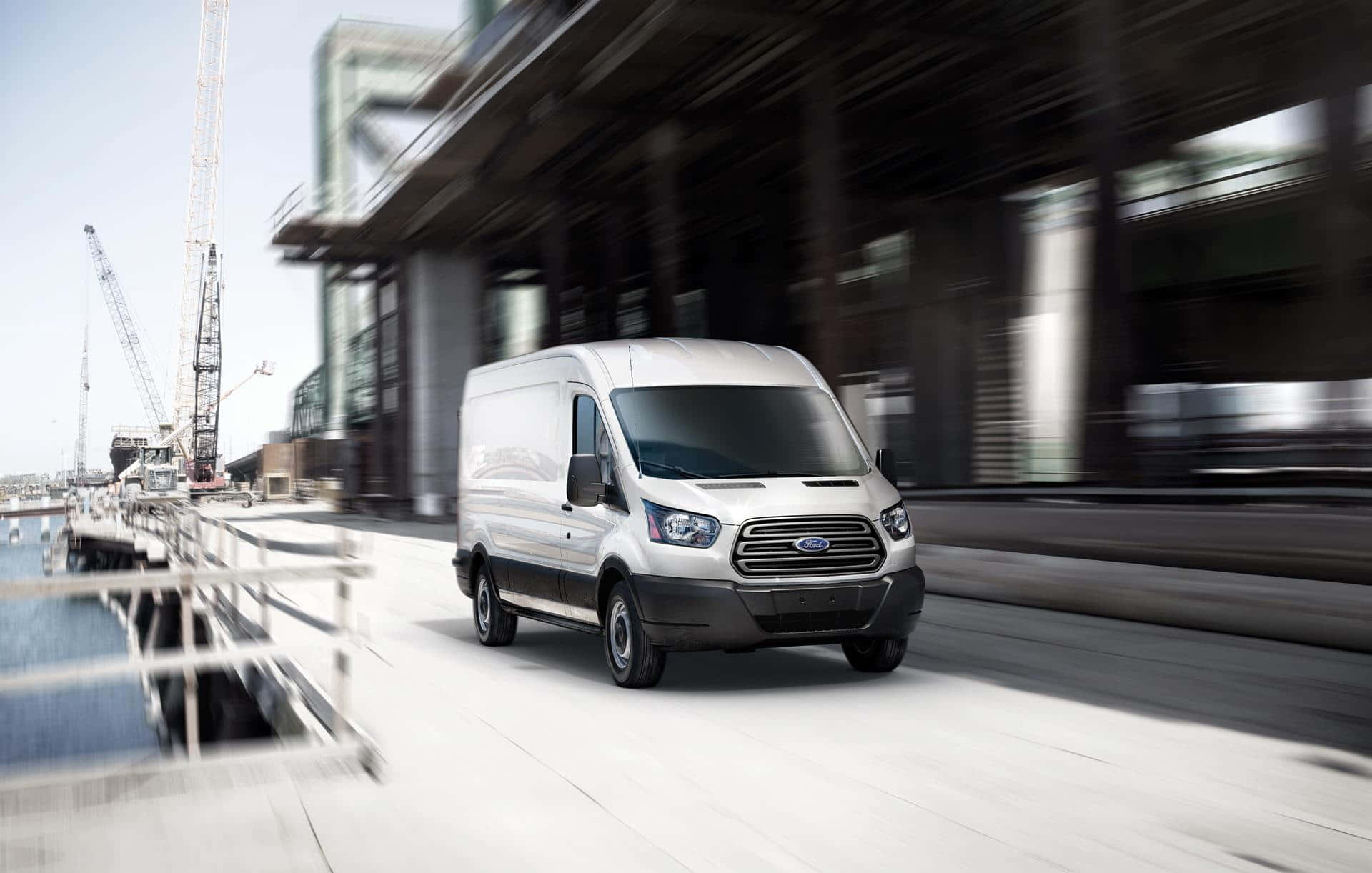 Ford Transit 桌布 壁紙 — 一輛白色福特全順廂型車沿著現代化海濱道路疾駛，在工業建築和起重機周圍產生動態模糊效果。