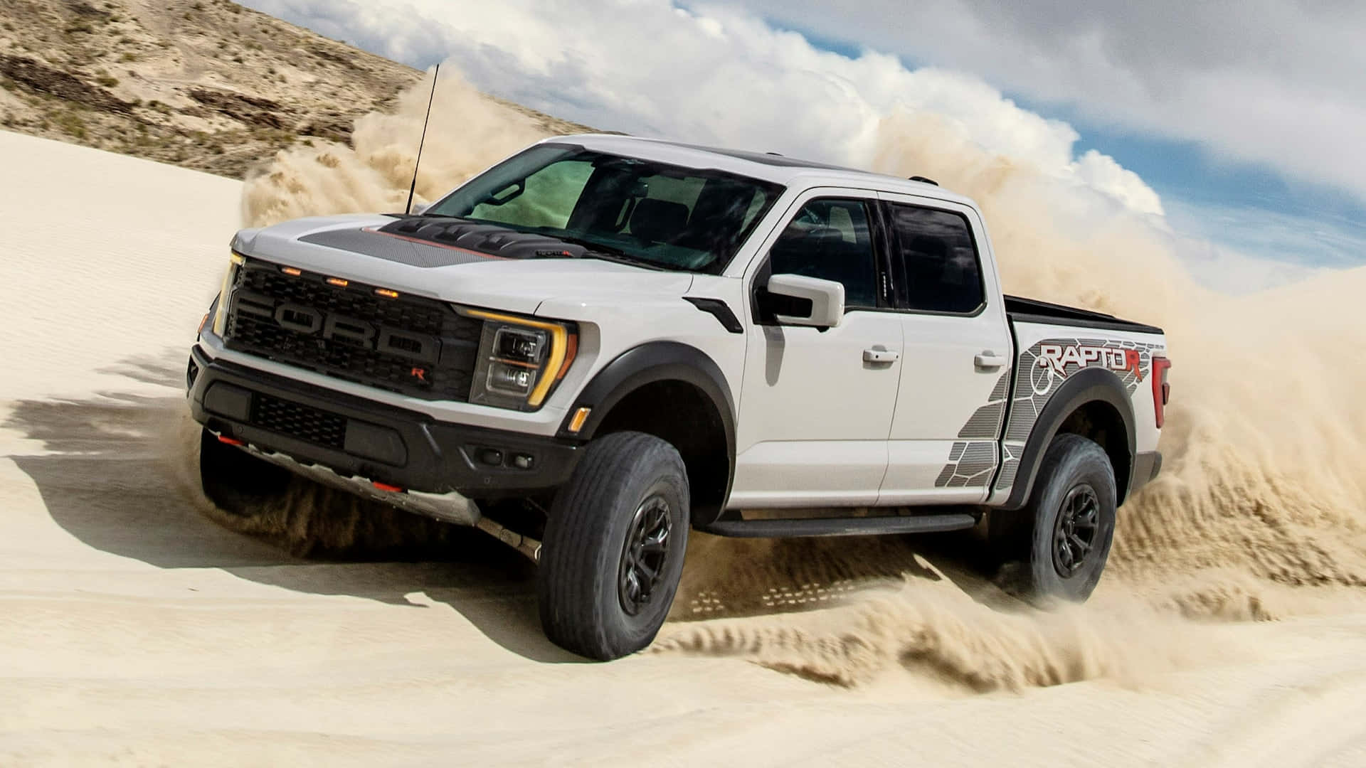 Ford F 150 桌布 壁紙 — 一輛白色福特猛禽卡車在陰天天空下，強力穿越沙漠沙丘，揚起沙塵。