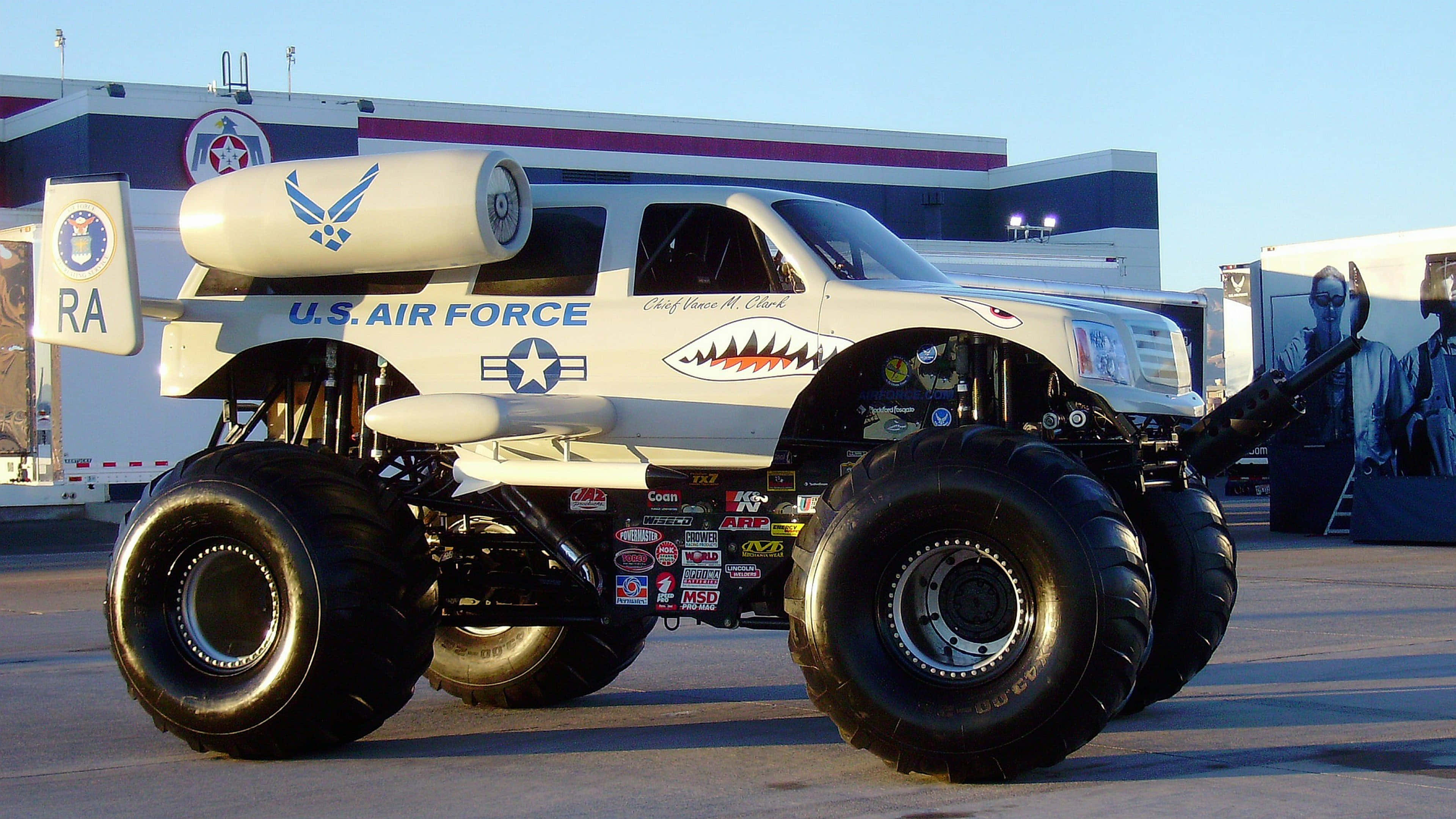 Air Force 桌布 壁紙 — 一輛白色美國空軍怪獸卡車，配備巨型輪胎和噴射引擎螺旋槳，在晴朗藍天下停泊於戶外活動場地。