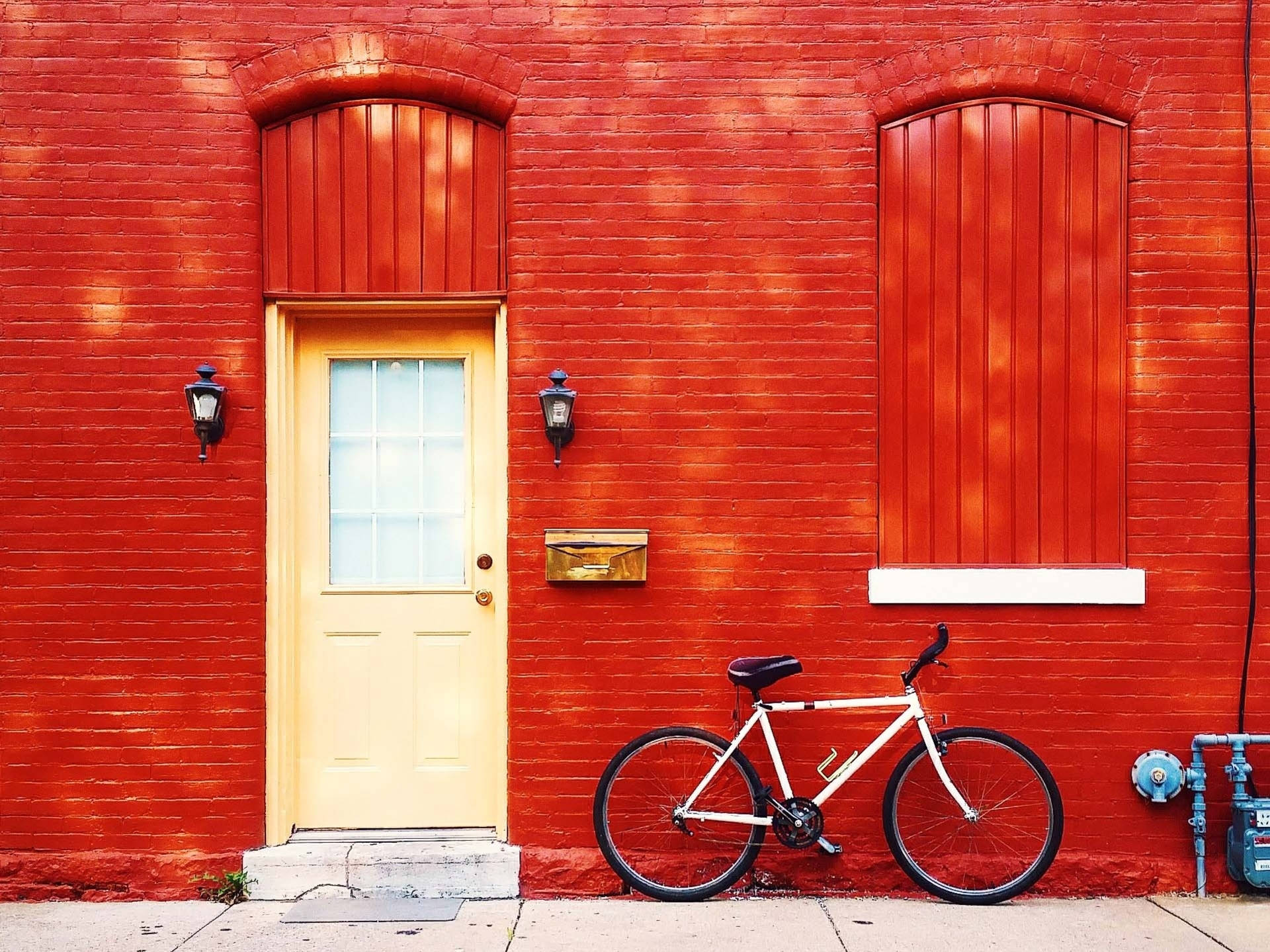 Bicycle 桌布 壁紙 — 一輛白色腳踏車靠在一面鮮紅色的磚牆旁，旁邊有一扇淺黃色的門，帶有拱形木工和復古燈籠。