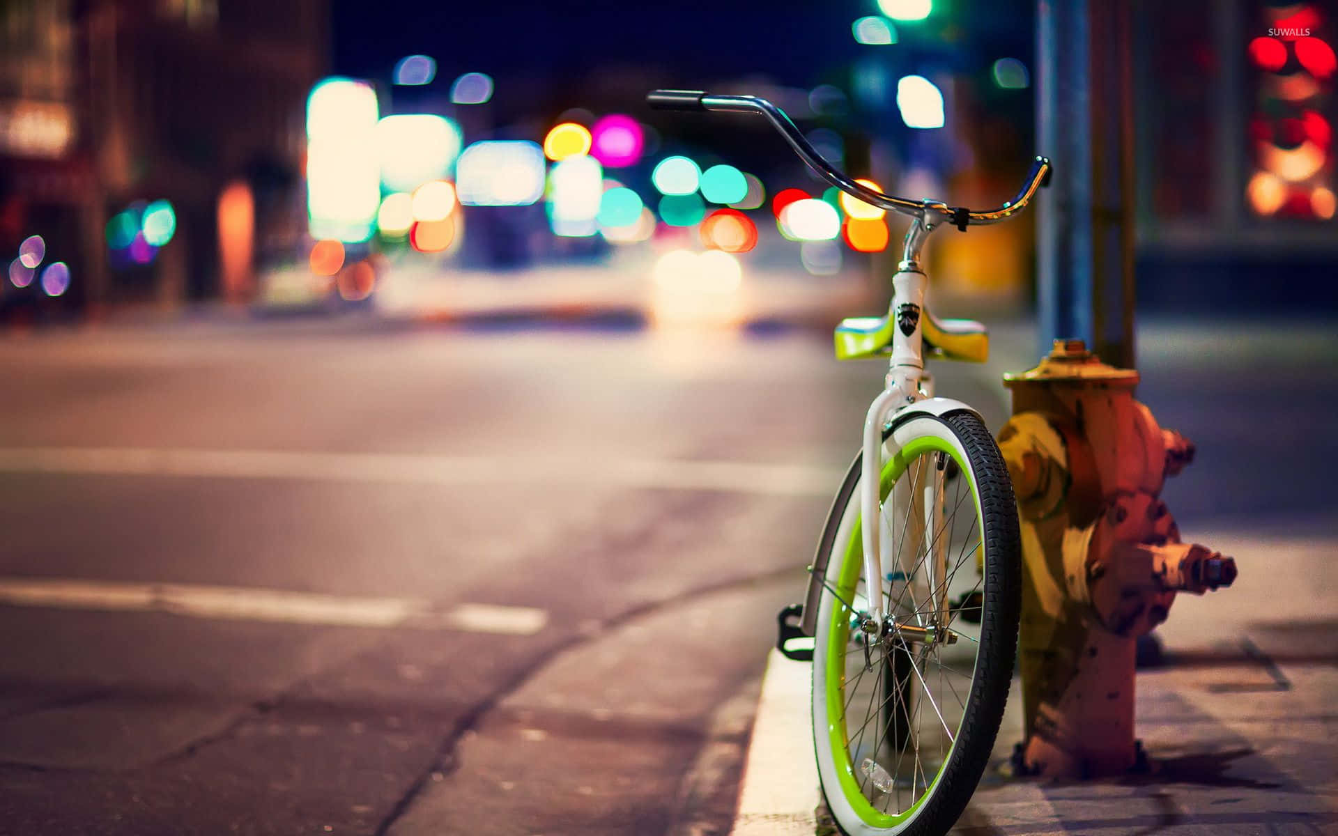 City Street 桌布 壁紙 — 一輛白色自行車配以螢光綠色車輪，在夜晚的城市街道上靠著黃色消防栓，背景有色彩繽紛的散景燈光。