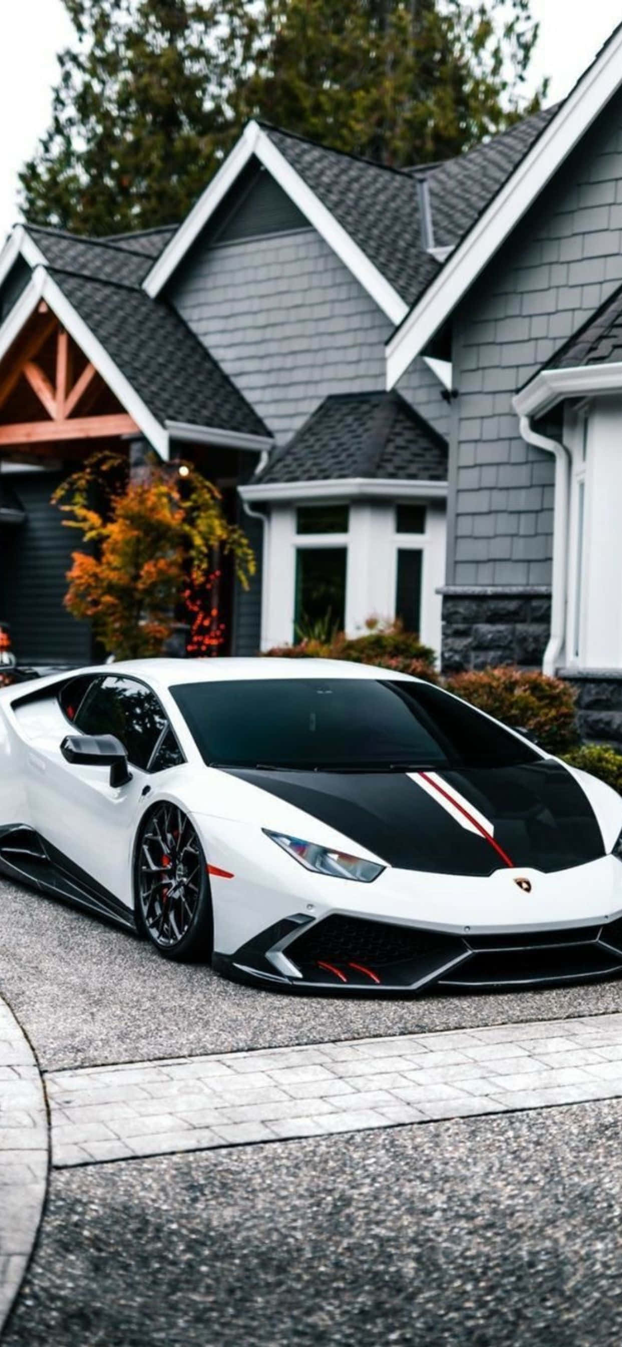 Lamborghini Phone 桌布 壁紙 — 一輛白色藍寶堅尼，帶有黑色和紅色點綴，停在現代灰色房屋前的石頭車道上，周圍有秋葉。