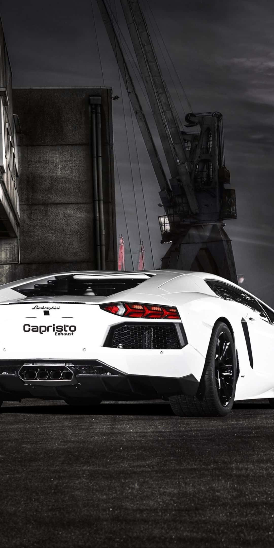 Pixel 3 Lamborghini 桌布 壁紙 — 一輛白色藍寶堅尼Aventador配備Capristo排氣管，夜間停泊在柏油路上，上方是深色工業起重機。