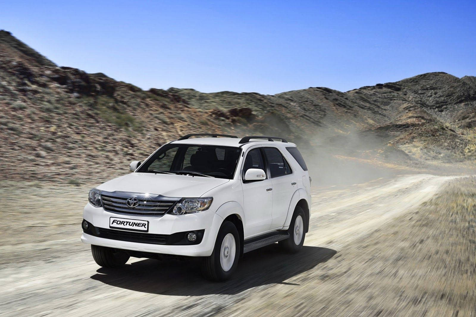 Scenery 桌布 壁紙 — 一輛白色豐田 Fortuner SUV 在塵土飛揚的沙漠道路上高速行駛，揚起沙塵，映襯著清澈的藍天。