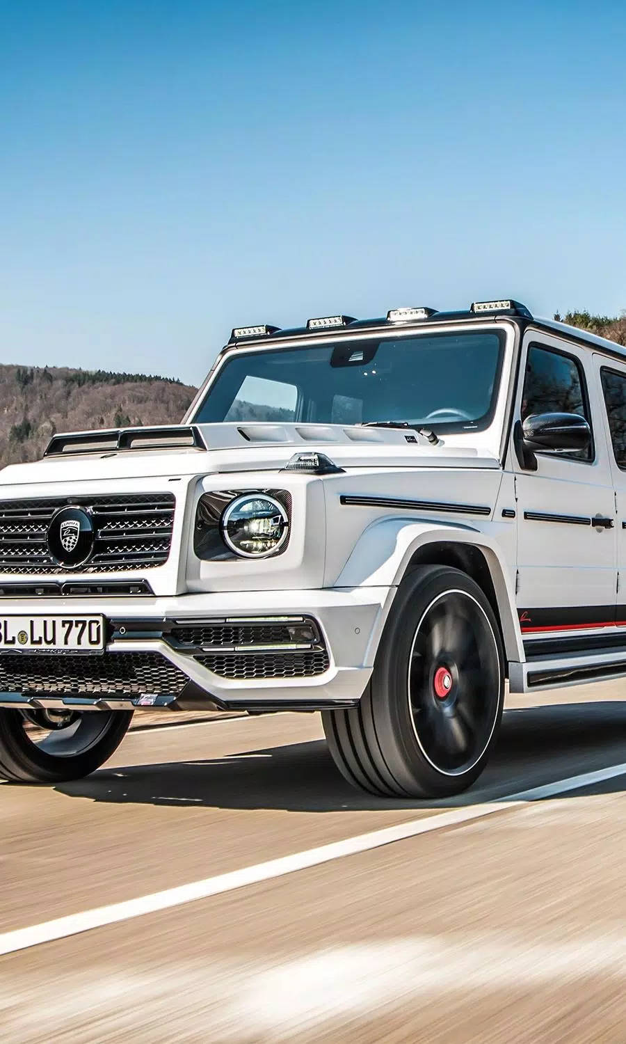Mercedes 桌布 壁紙 — 一輛白色豪華SUV在陽光明媚的道路上行駛，帶有模糊的動態效果，背景是晴朗的藍天和遠山。