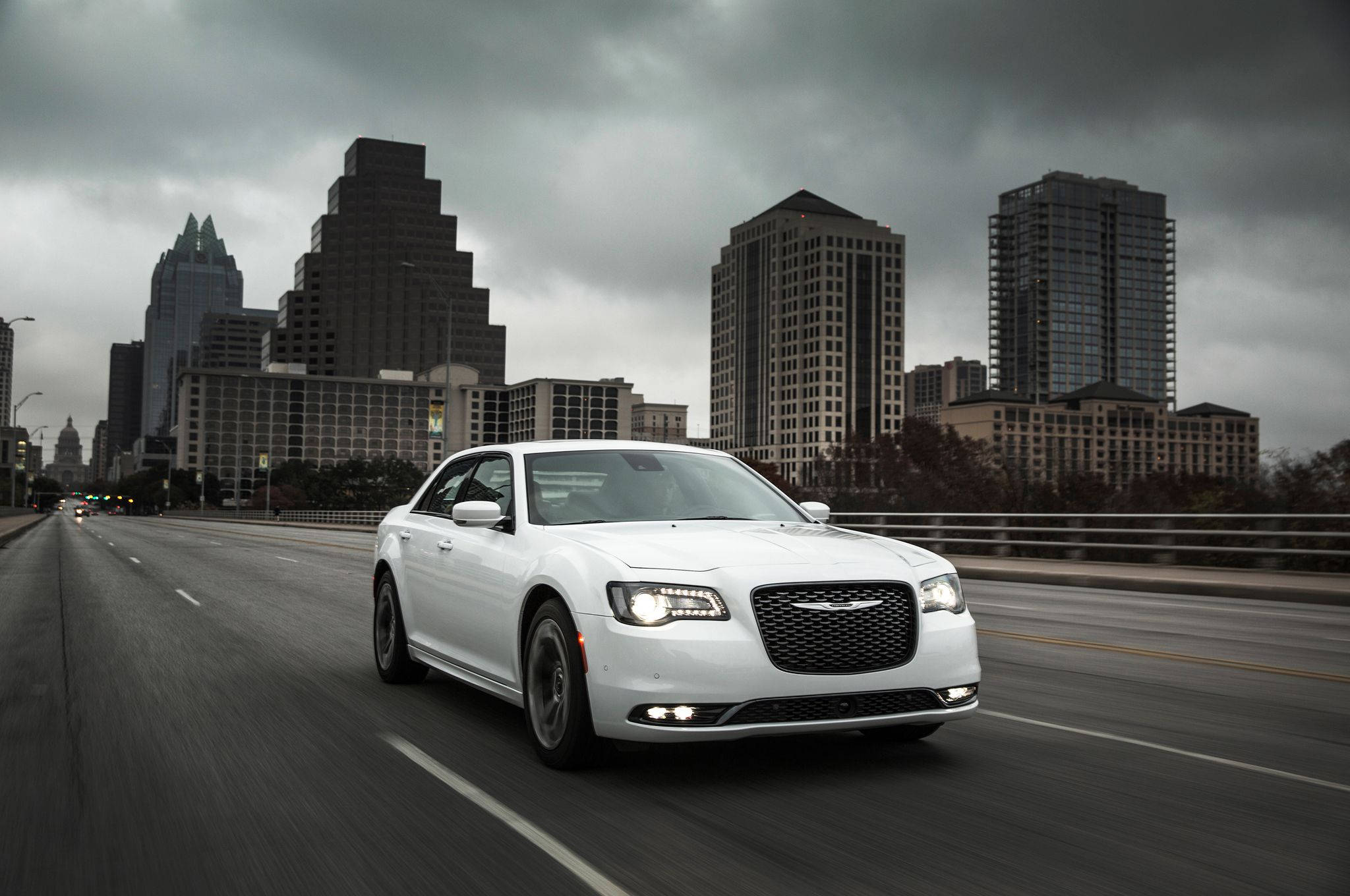 Chrysler 桌布 壁紙 — 一輛白色豪華轎車在陰天之下疾馳過橋，背景是現代城市天際線。